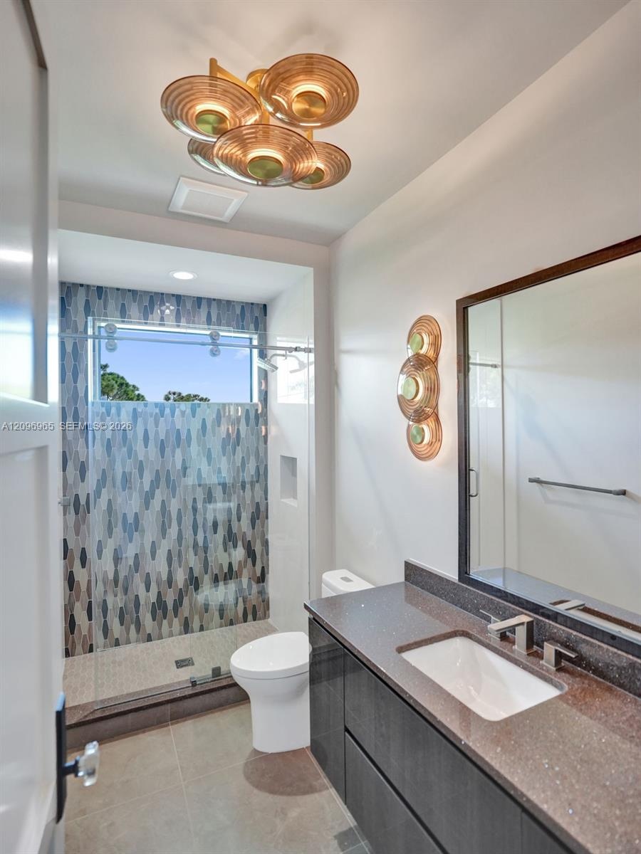 Modern vanity with stone countertop and integrated sink, frameless glass shower enclosure featuring patterned tile surround, and contemporary metallic