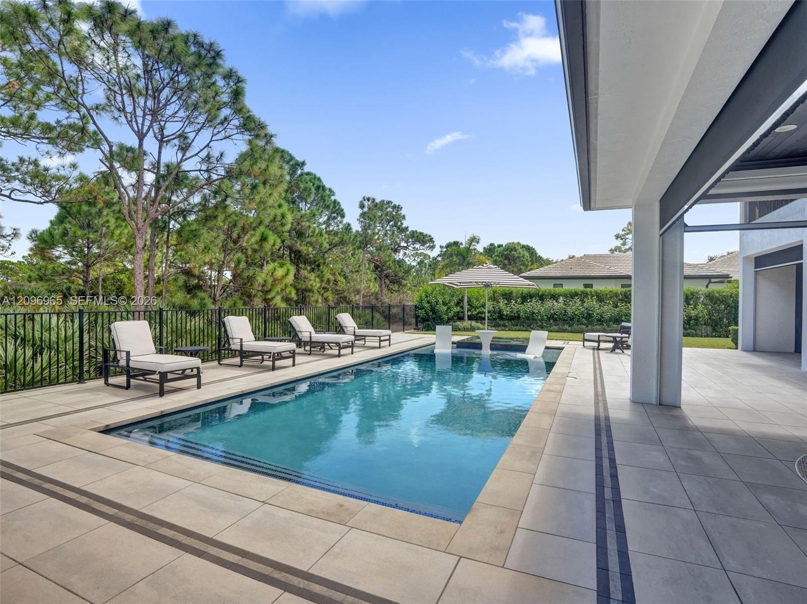 Rectangular swimming pool featuring a tanning ledge, travertine-style tiled deck, and black metal perimeter fencing