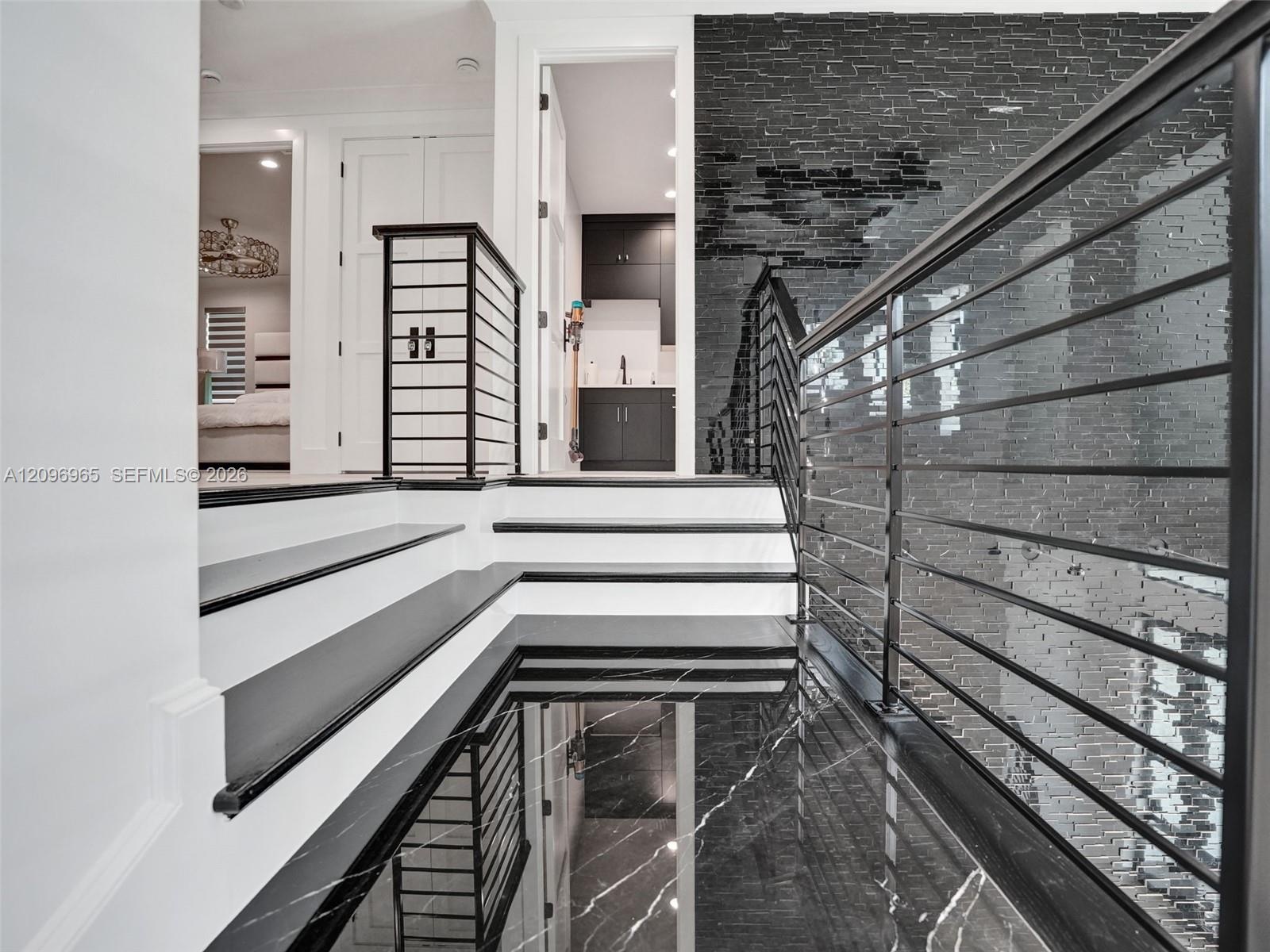 Staircase featuring dark stone treads, a metal horizontal-bar railing, and a textured black brick accent wall