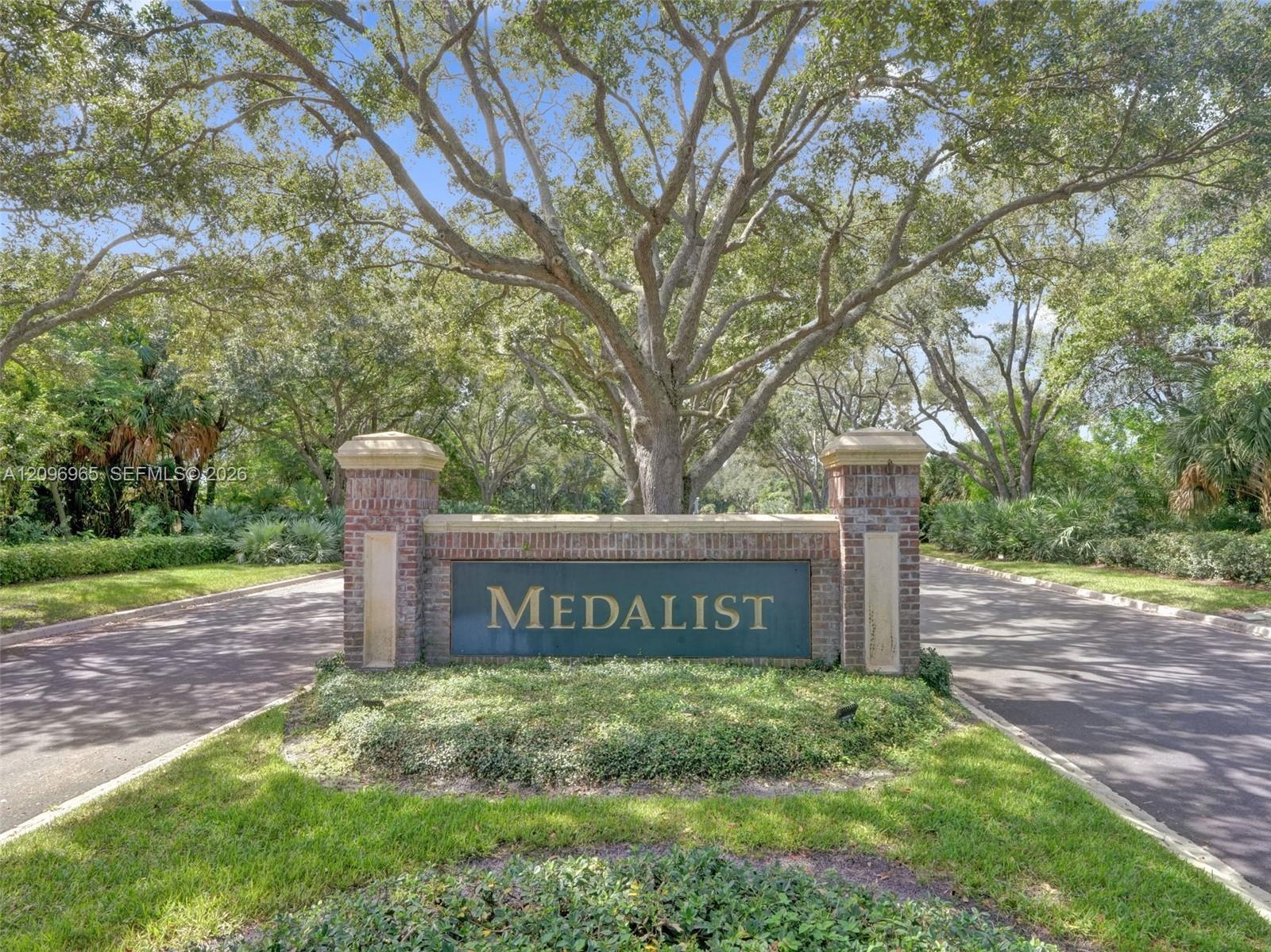 Brick monument signage featuring stone accents, surrounded by mature trees, landscaping, and paved roadway access