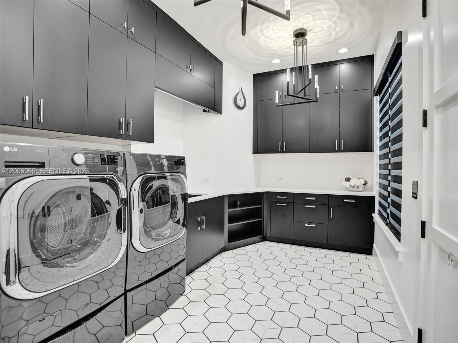 Laundry room featuring floor-to-ceiling matte black cabinetry, contrasting white countertops, geometric hexagonal floor tile, and modern geometric ove