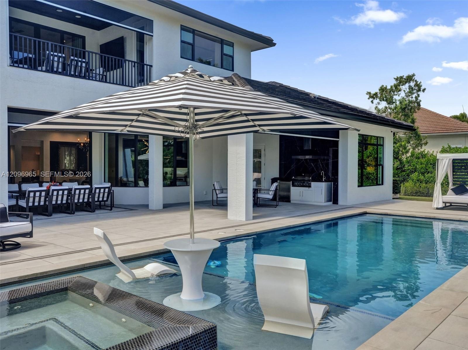 Swimming pool featuring a sun shelf with a built-in table, integrated spa, covered patio, and outdoor kitchen