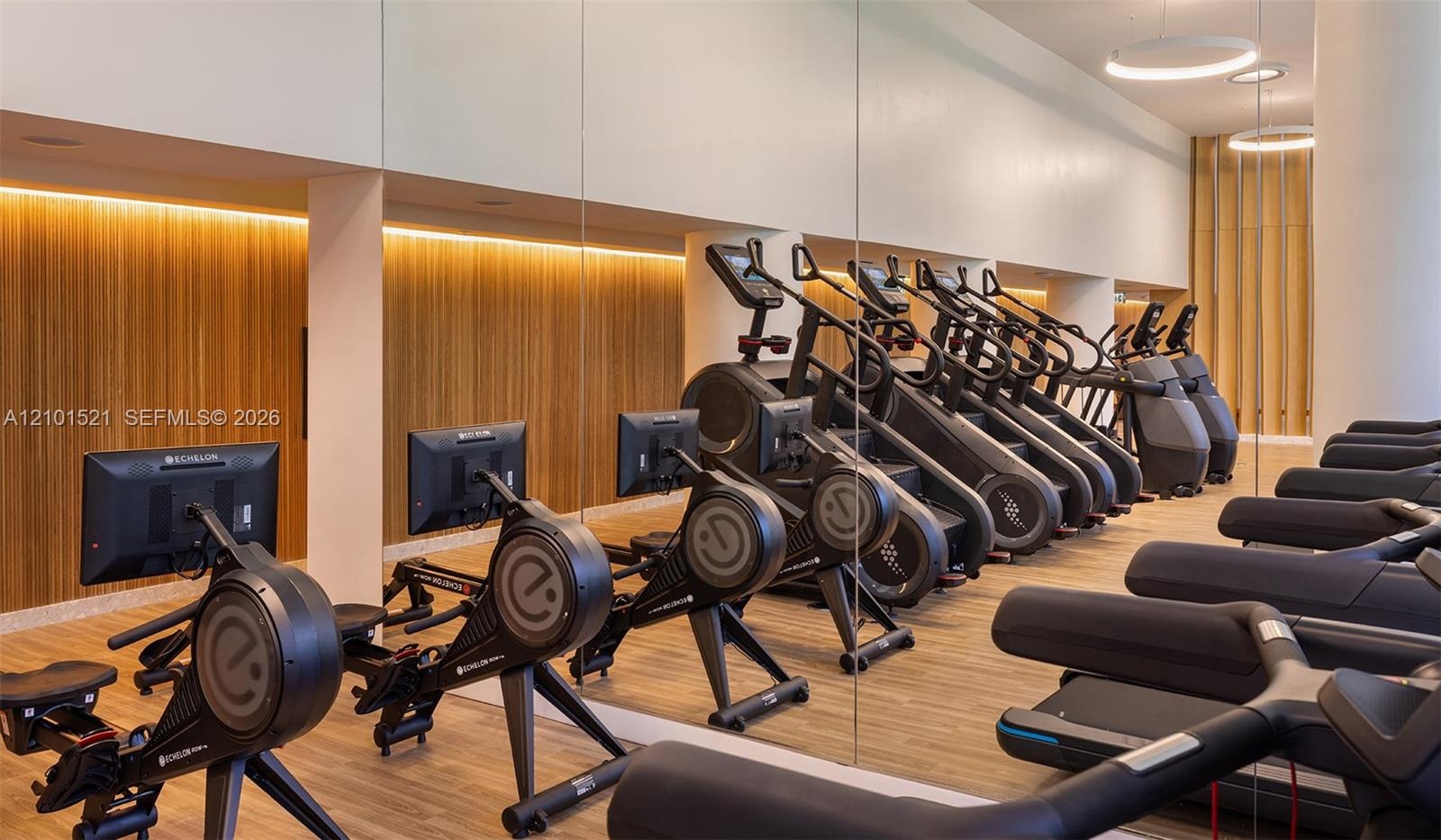 Fitness center featuring floor-to-ceiling mirrored walls, wood-panel accent walls, integrated cove lighting, circular pendant light fixtures, and wood