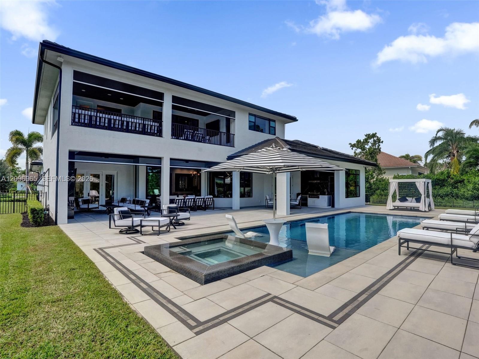 Two-story stucco exterior featuring a covered patio, second-level balcony, heated pool with in-water lounging shelf, and integrated spa