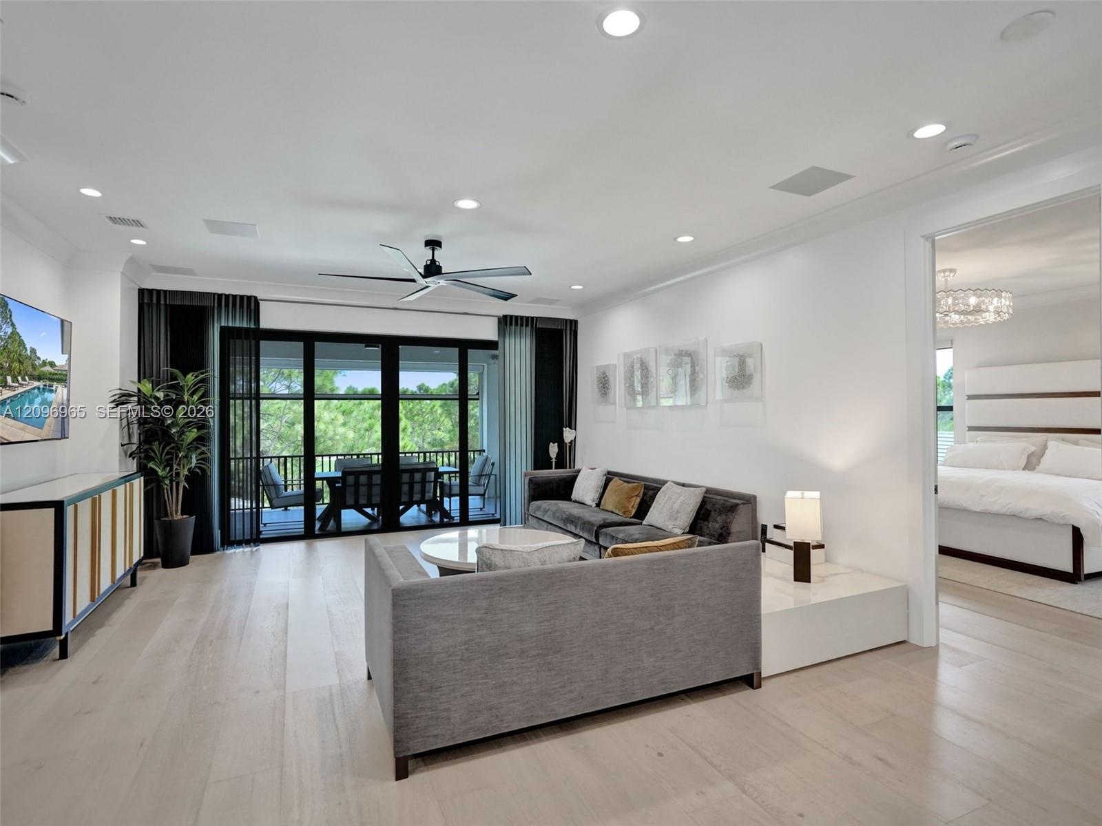 Open-concept interior featuring light wood-finish flooring, recessed lighting, a modern ceiling fan, and black-framed glass sliding doors opening to a