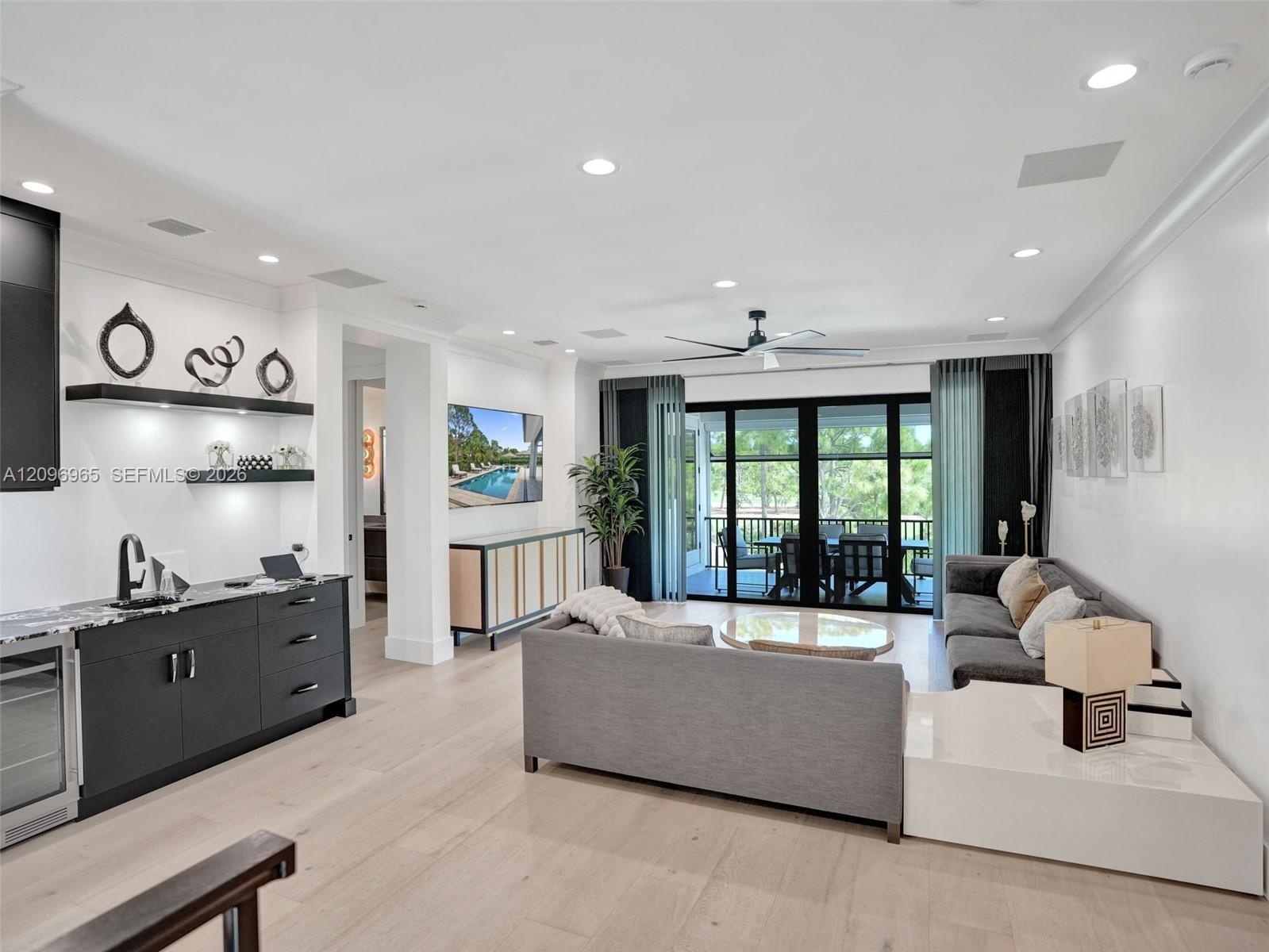 Living area featuring wood-finish flooring, recessed lighting, a ceiling fan, and a built-in wet bar with dark cabinetry and stone countertops