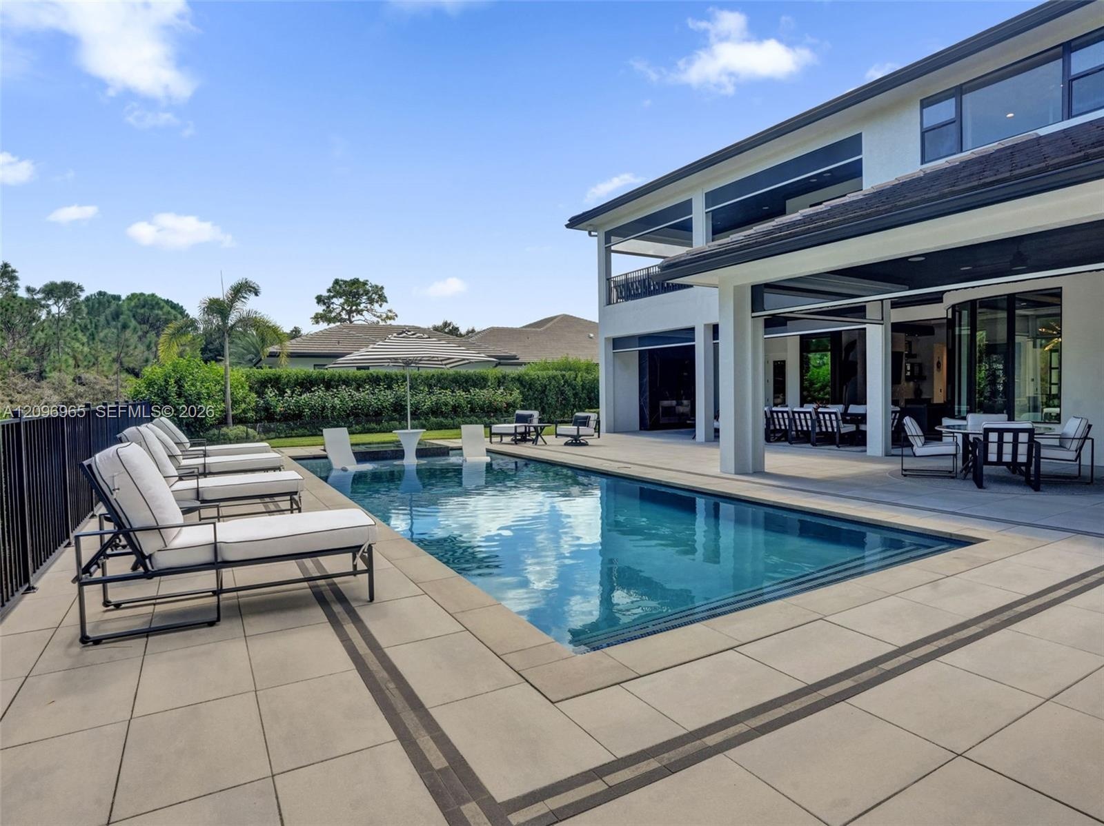 Outdoor living area featuring a custom swimming pool with a built-in sun shelf, expansive stone-paver decking, and a covered lanai