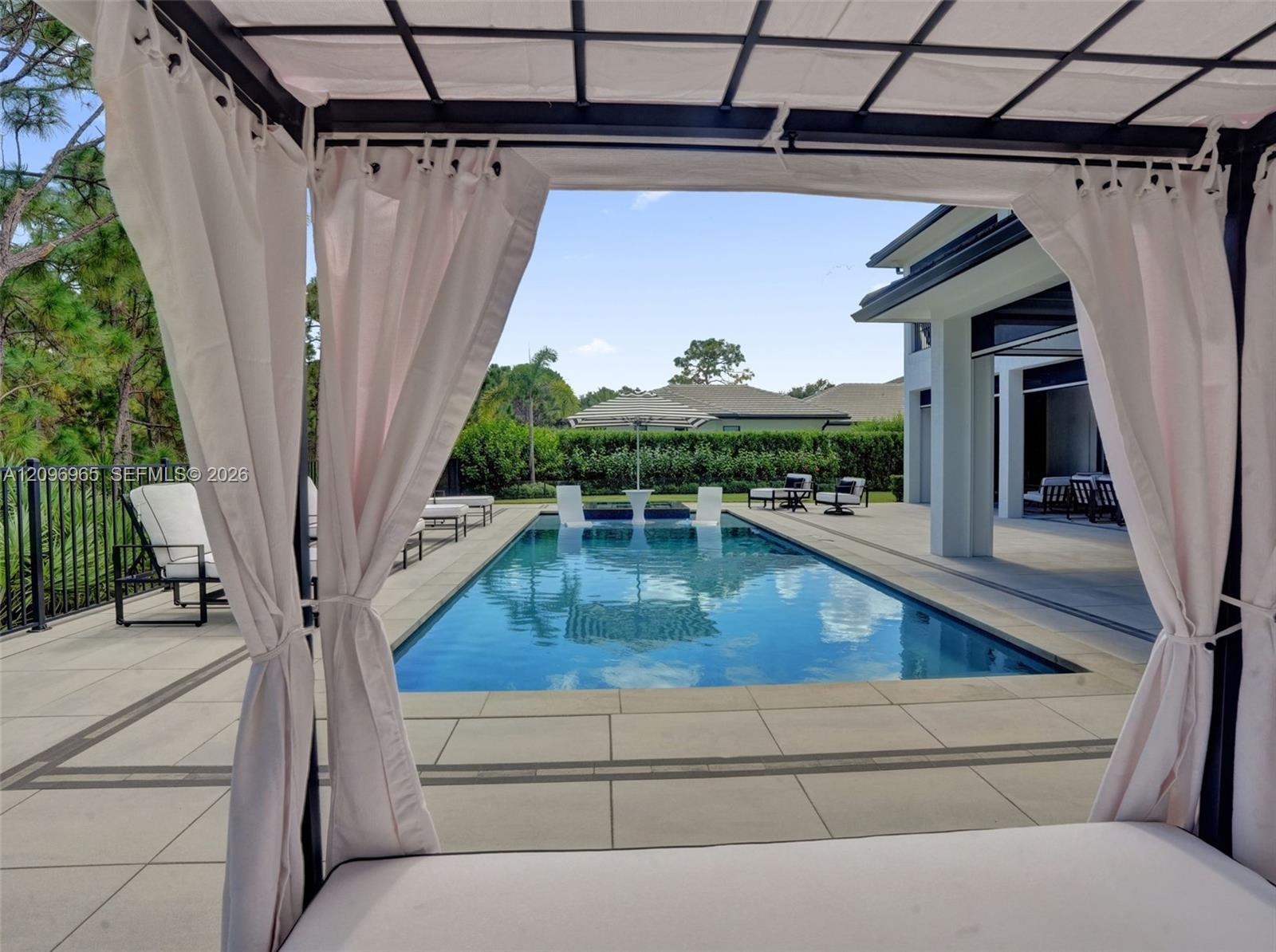 Rectangular swimming pool featuring a Baja shelf, paved stone deck, metal perimeter fencing, and a built-in covered cabana structure