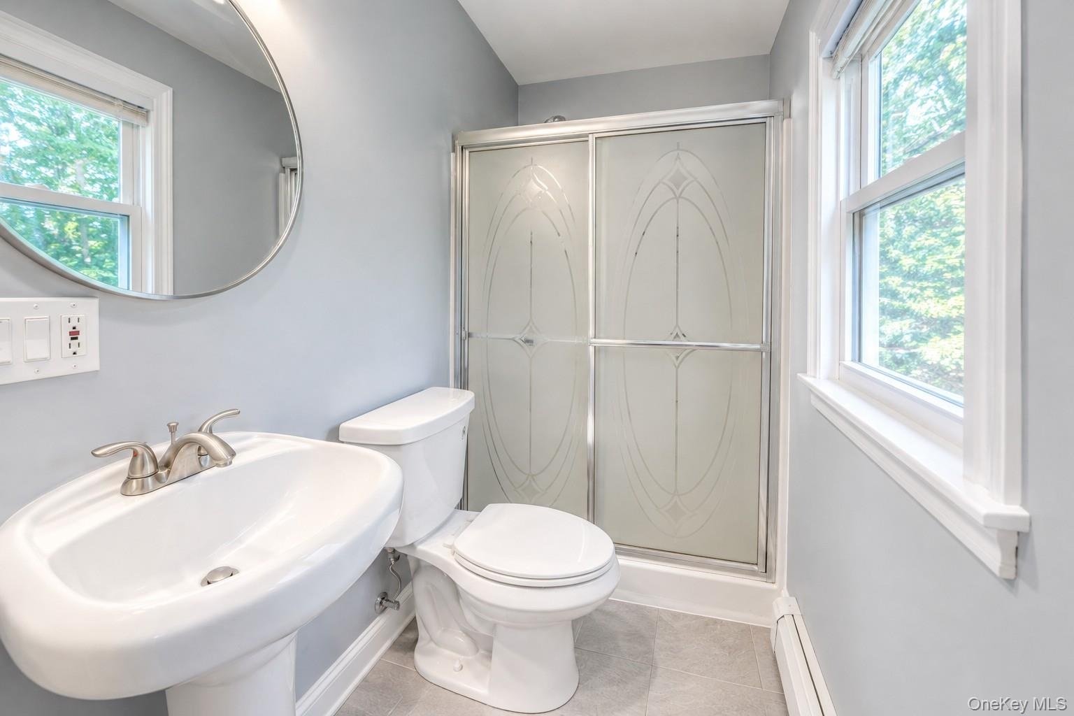 Bright, modern bathroom featuring a pedestal sink with brushed-nickel fixtures, a round mirror, and a frosted glass shower enclosure with decorative e