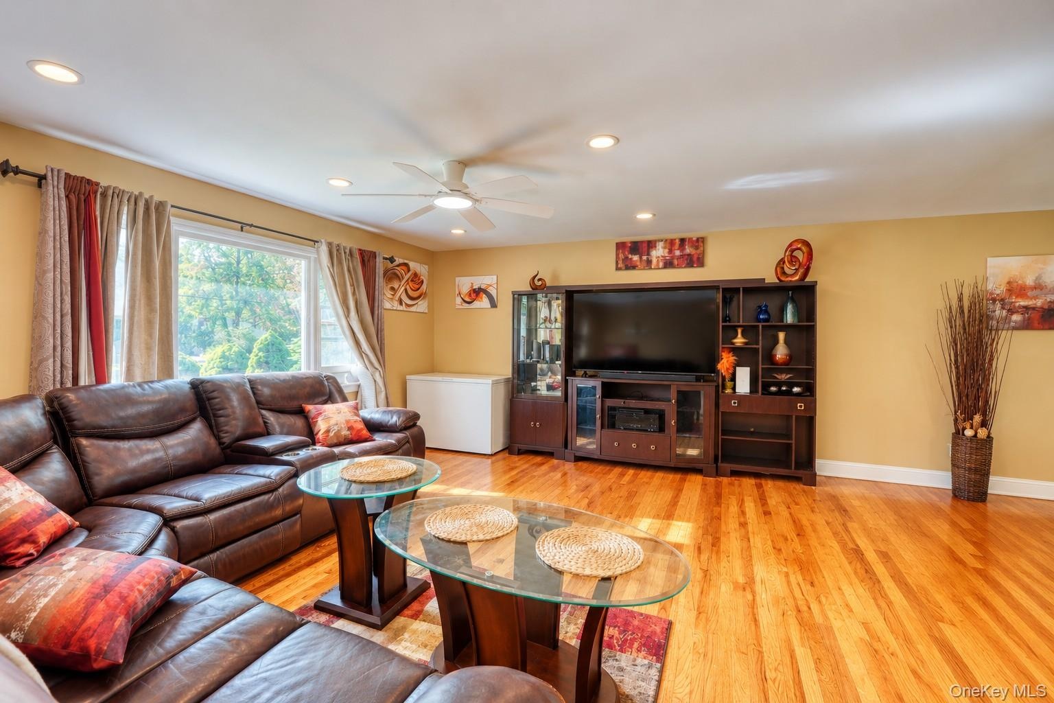 Inviting living room featuring rich hardwood floors, warm neutral walls, and a large picture window that fills the space with natural light. The room 