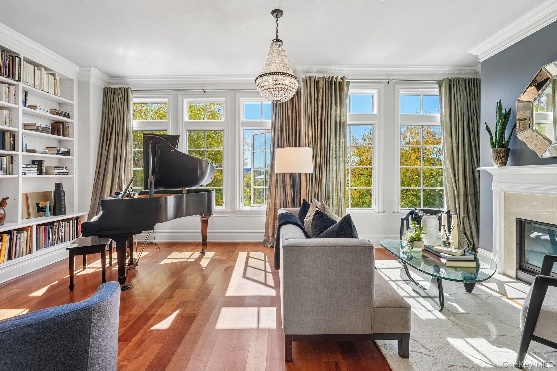 Hardwood-style flooring throughout, built-in shelving, fireplace with stone surround, crown molding, and a crystal chandelier