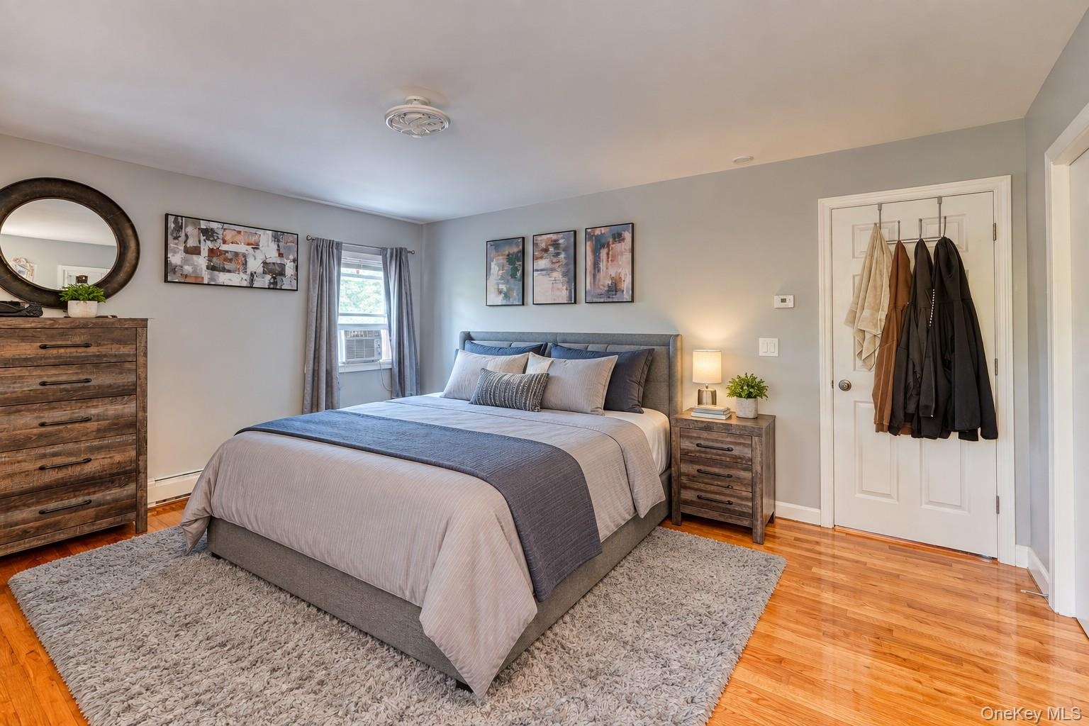 Inviting primary bedroom featuring warm hardwood floors, soft gray walls, and abundant natural light. The space includes a plush area rug, modern wood