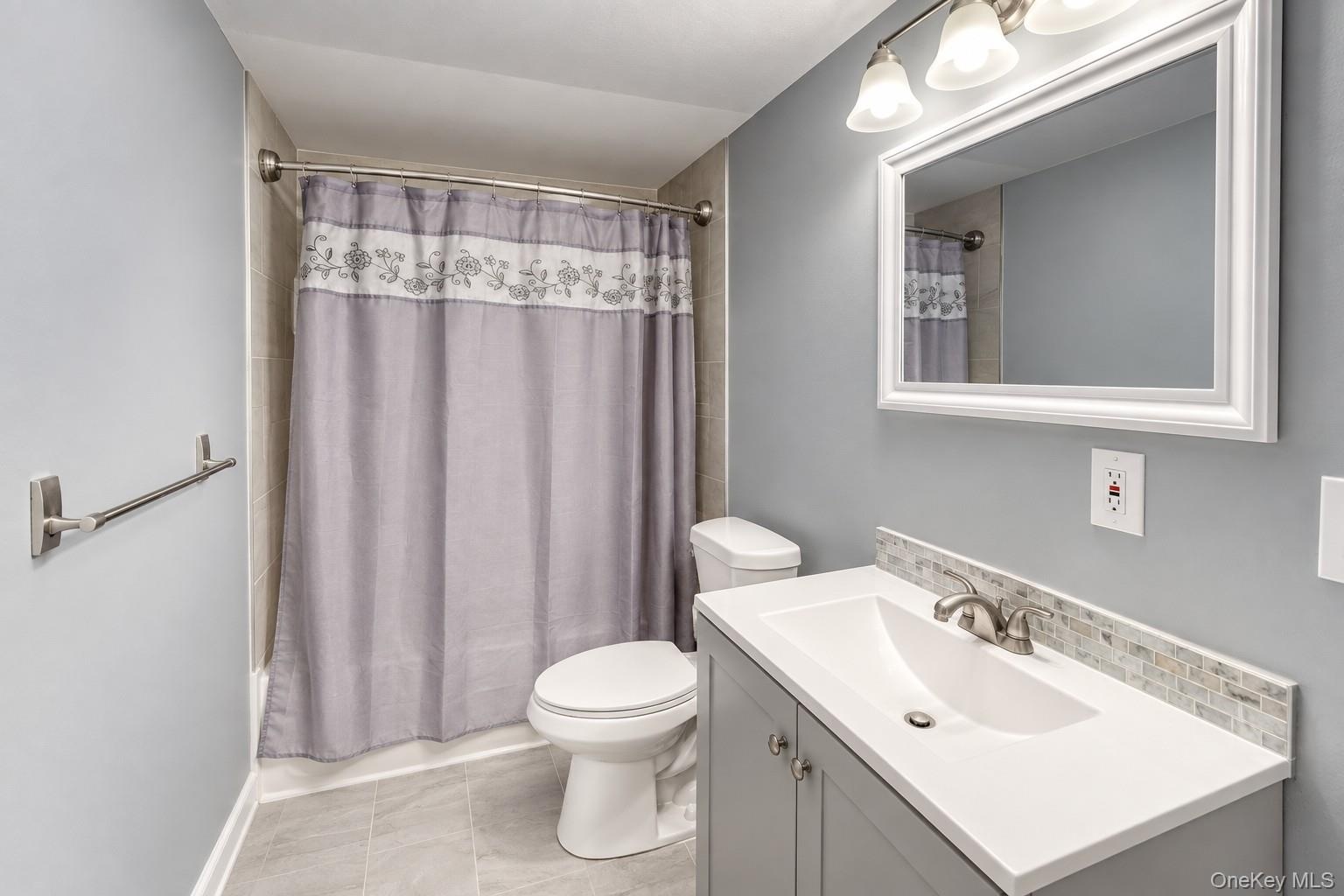 Stylish full bathroom featuring a modern vanity with brushed-nickel fixtures, white framed mirror, and elegant tile backsplash. The space is accented 