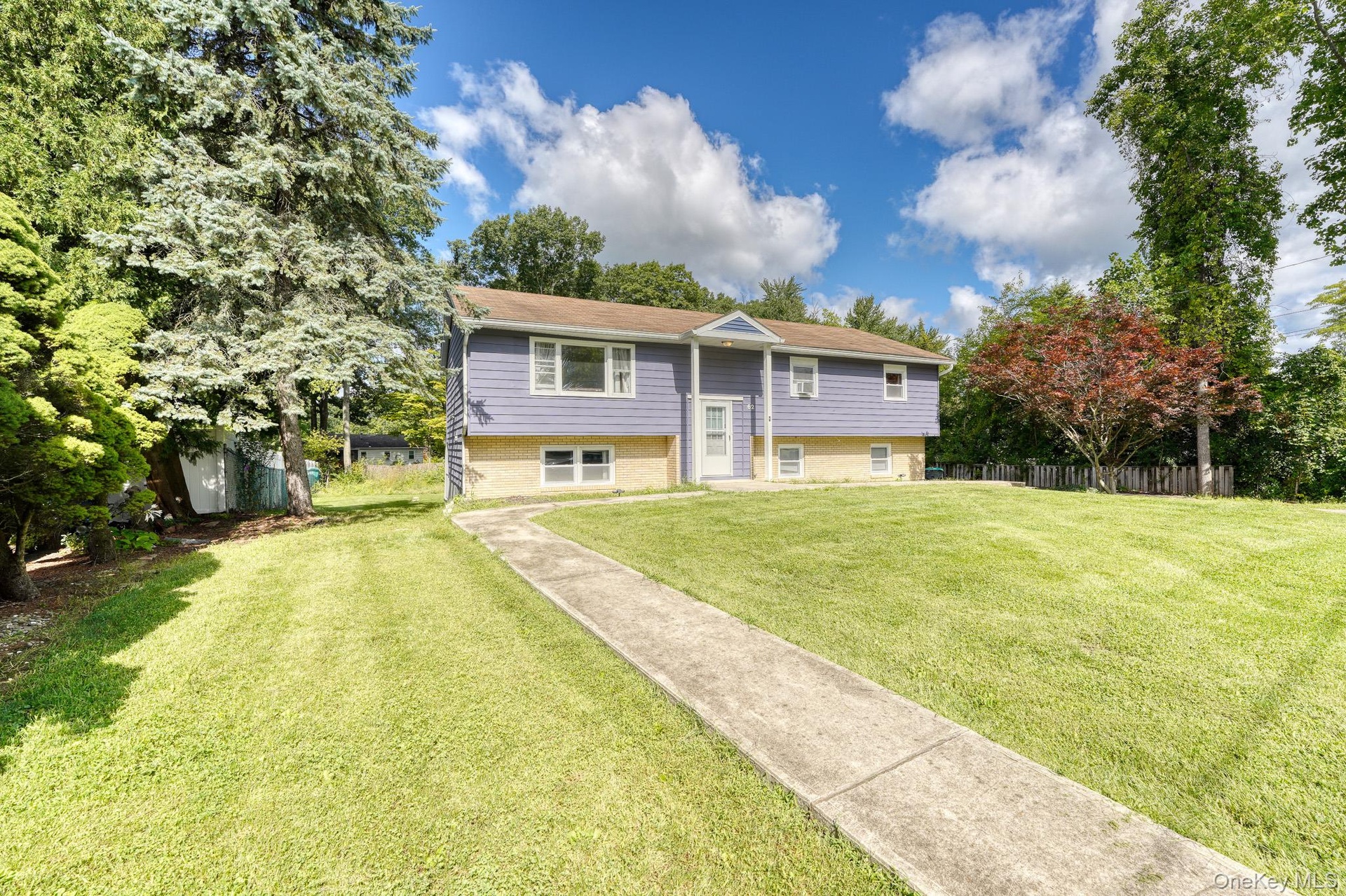 Charming split-level home with a welcoming front entrance and manicured lawn. The exterior combines light brickwork with blue siding for a modern yet 