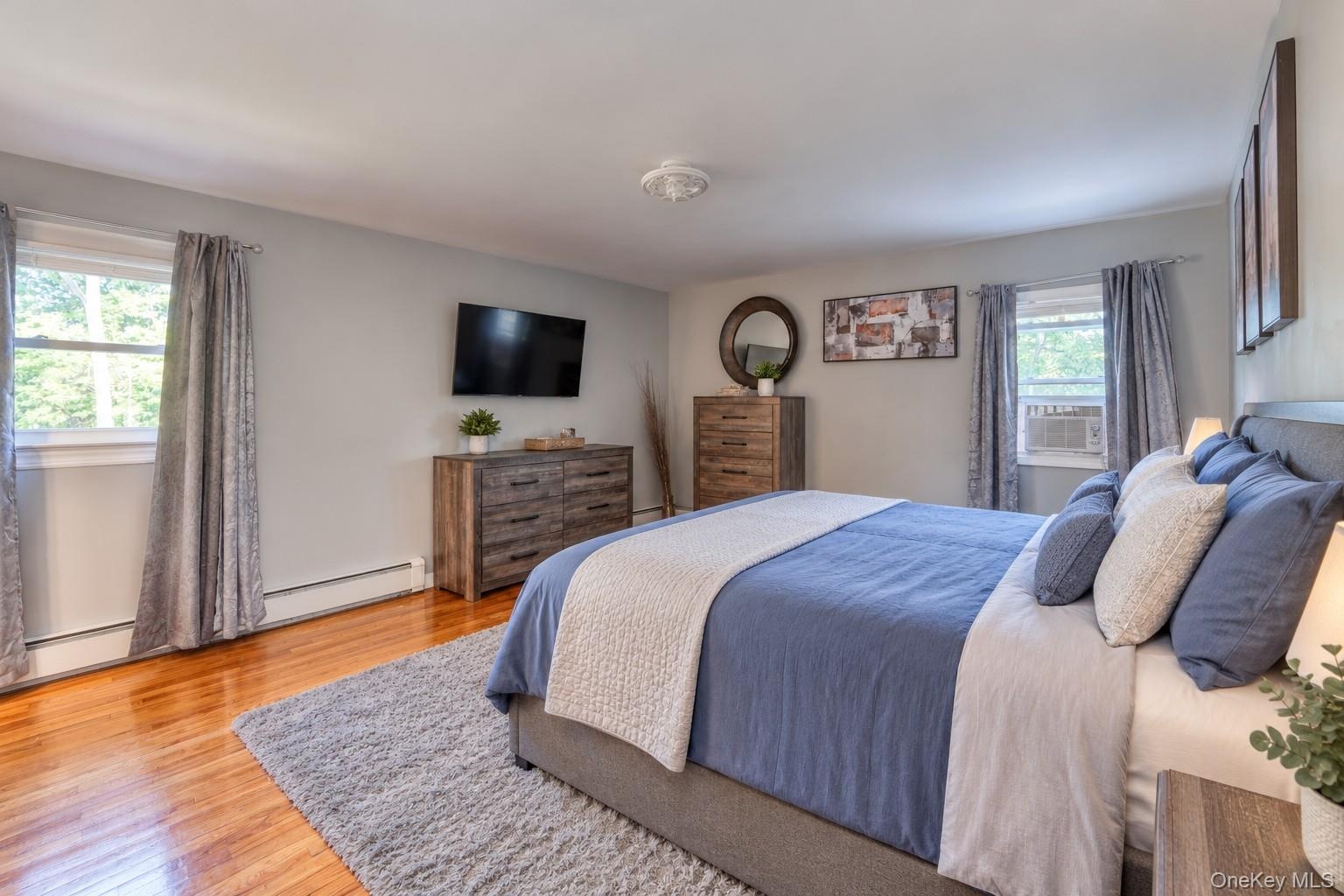 Spacious primary bedroom with en-suite bath, featuring warm hardwood floors and soft gray walls for a serene atmosphere. The room includes a large uph