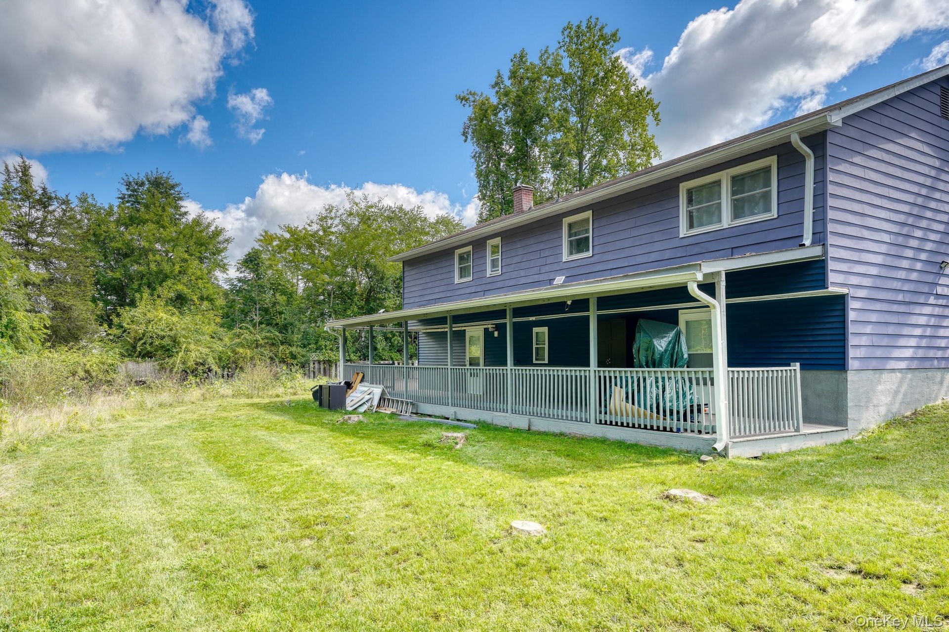 Expansive backyard featuring a large, covered porch that spans the length of the home — perfect for outdoor relaxation or entertaining. The home’s blu