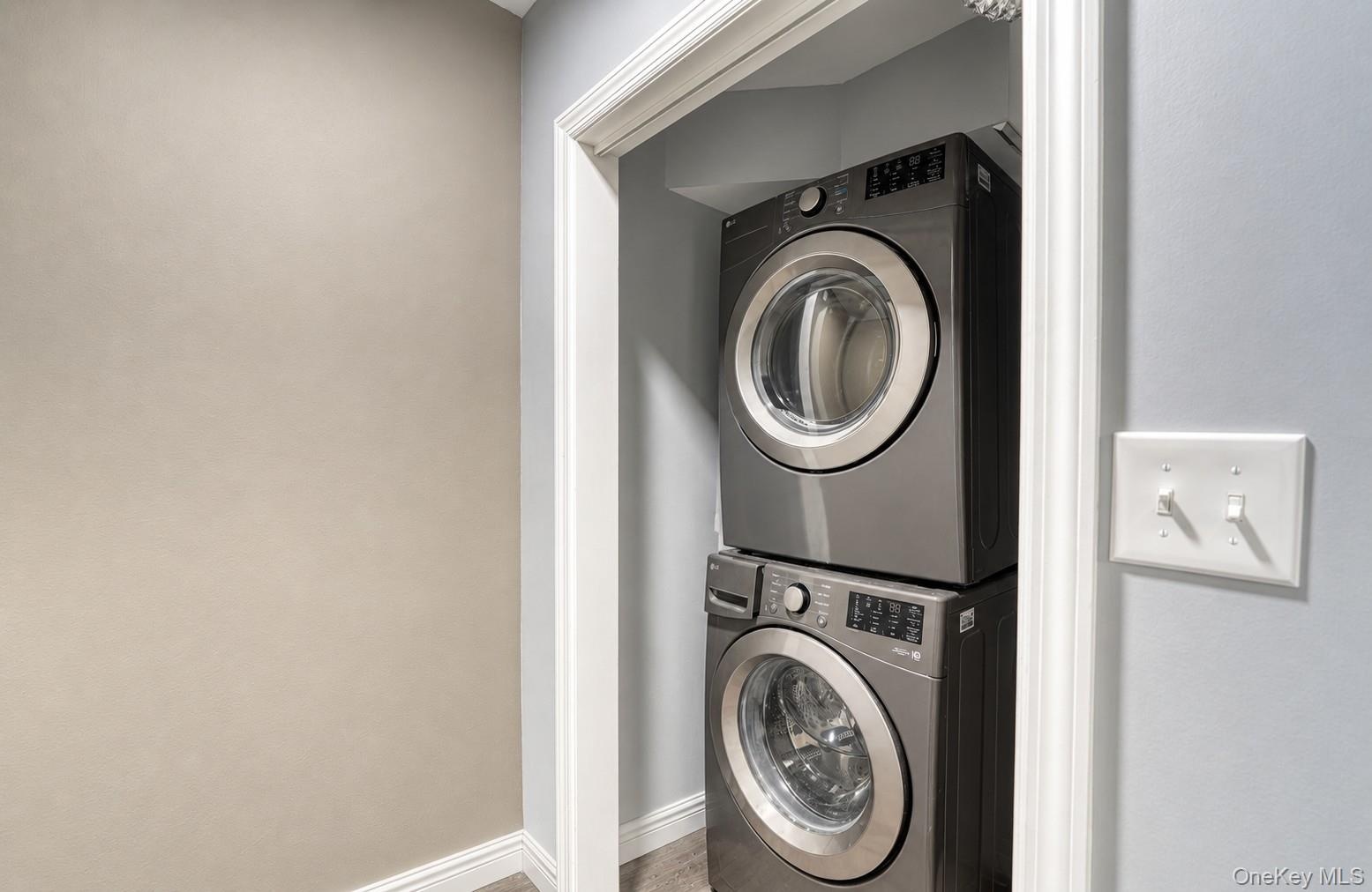 Compact and efficient laundry nook featuring a modern stacked washer and dryer set in a recessed space with clean white trim. The sleek metallic finis