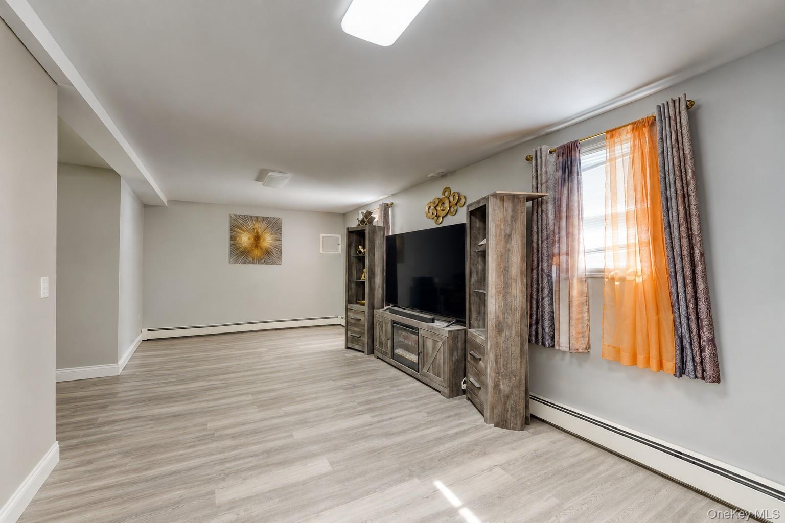 Spacious and modern family room featuring light gray walls, wide-plank flooring, and a rustic entertainment center with built-in shelving and a large 