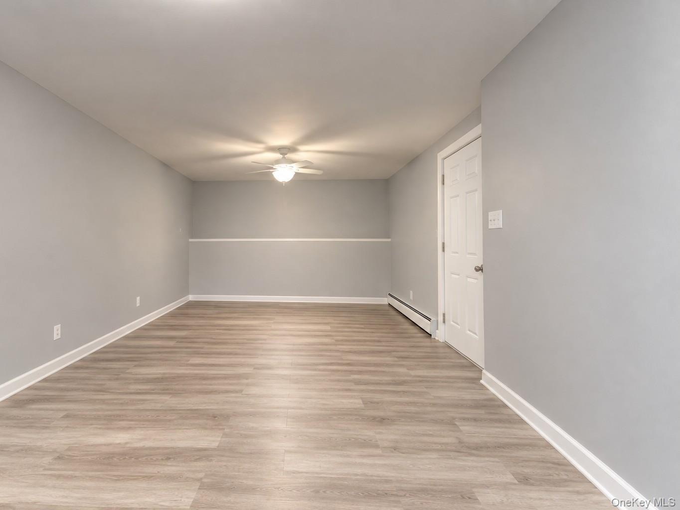 Spacious finished room featuring light gray walls, wide-plank vinyl flooring, and crisp white trim for a clean, modern look. The ceiling fan with inte
