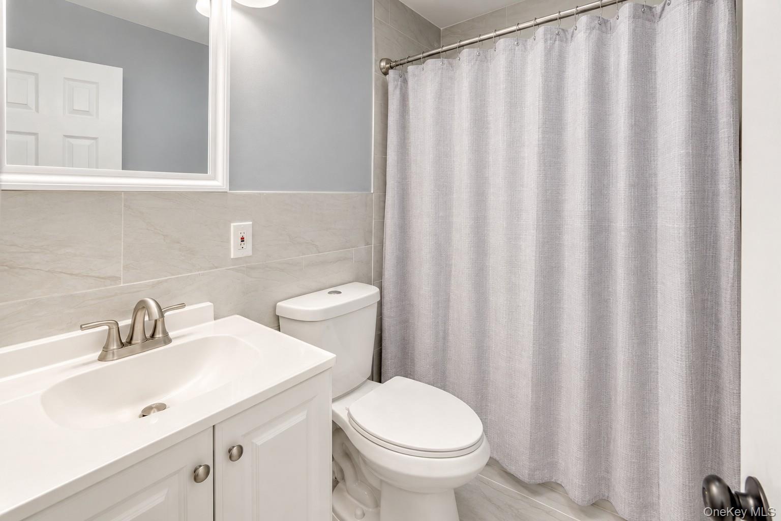Modern full bath featuring a white vanity with brushed-nickel fixtures, matching hardware, and a sleek integrated sink. Light gray tile walls and floo