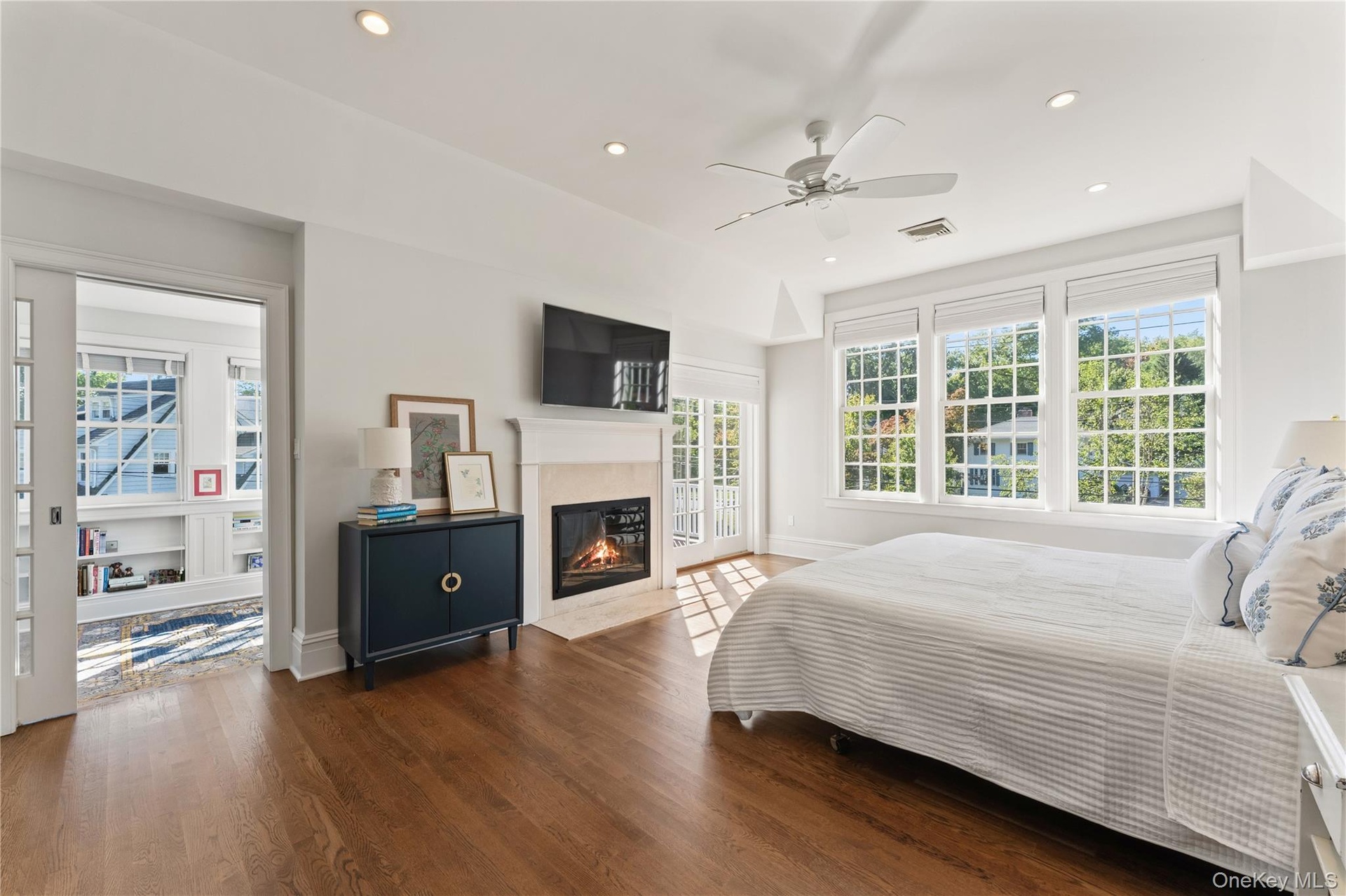Luxurious sun-filled primary suite with gas fireplace, a pocket door for privacy to a window-lined office/sunroom and a door to the deck for outdoor r