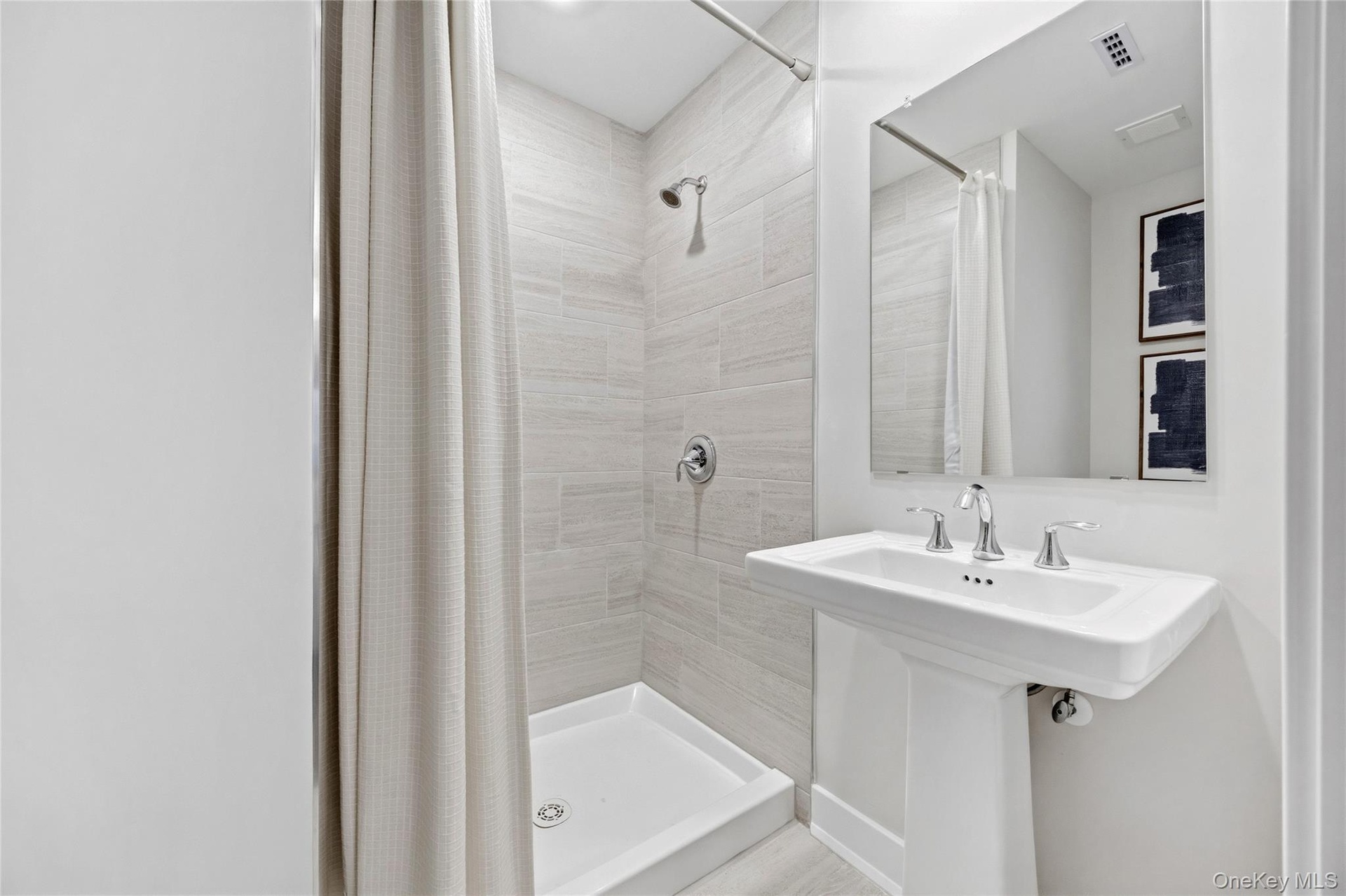 Basement Full Bathroom. Pedestal sink with chrome fixtures, a framed mirror, and a shower with light-toned wall tile