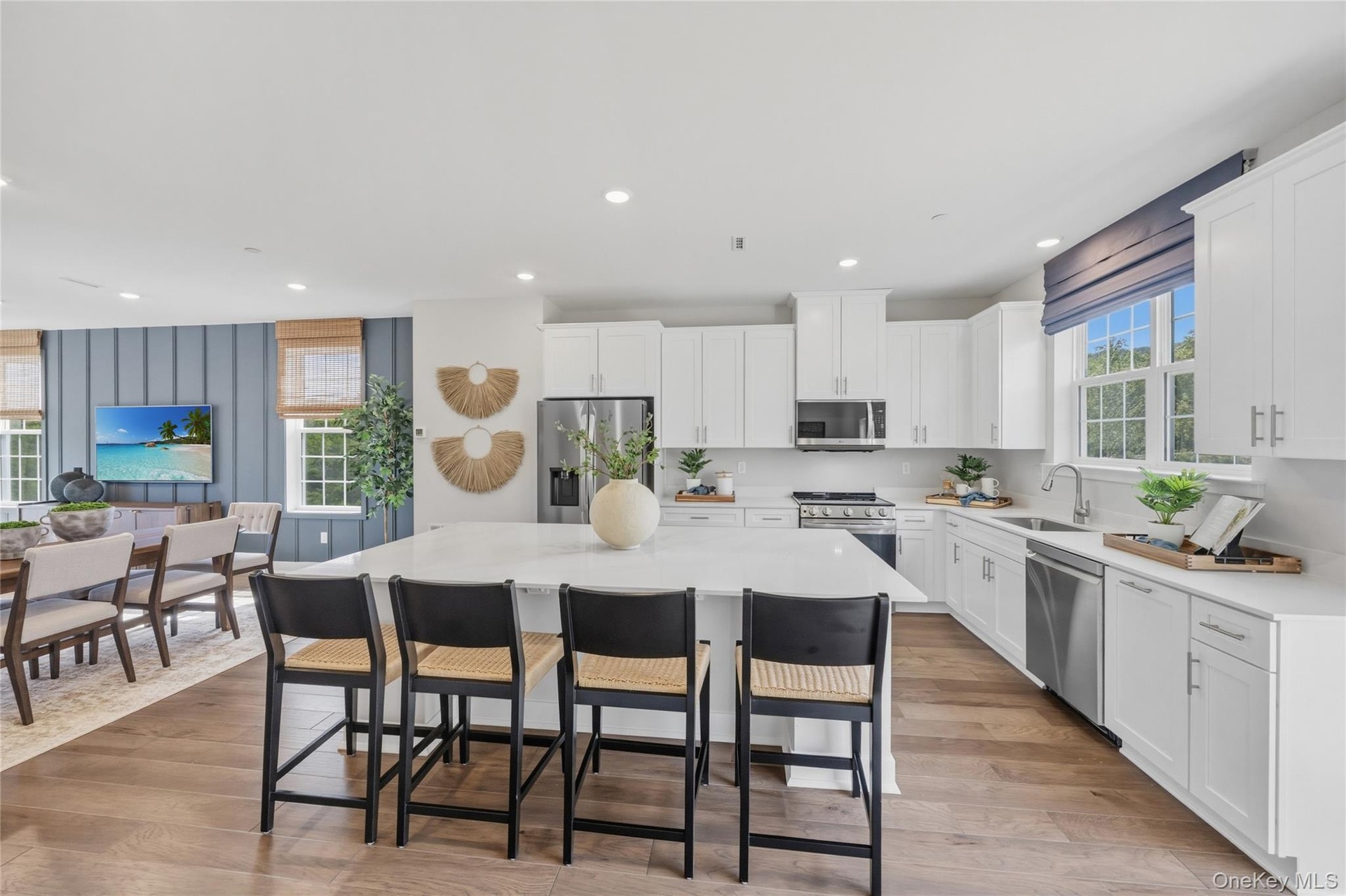 Open-concept kitchen featuring an spacious island with seating, white shaker cabinetry, stainless steel appliances, and wood-finish flooring
