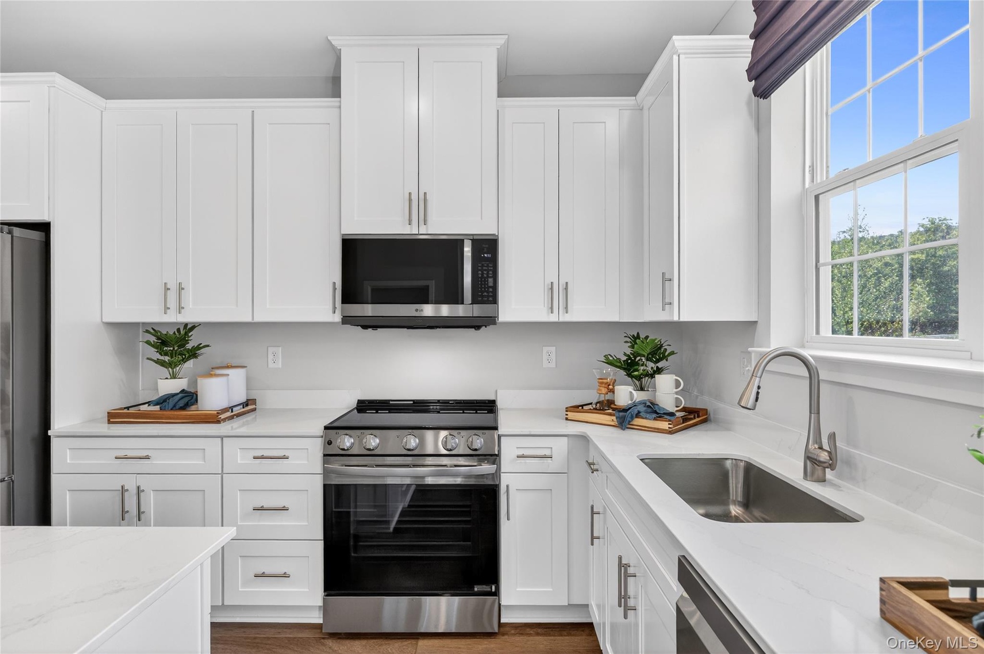 Modern kitchen featuring white shaker cabinetry, stainless steel appliances, light-toned countertops, and a stainless steel sink with a gooseneck fauc