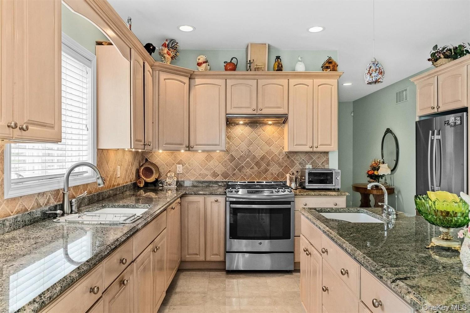 Kitchen with light wood finish cabinets, dark stone countertops, stainless steel appliances, and pendant lighting