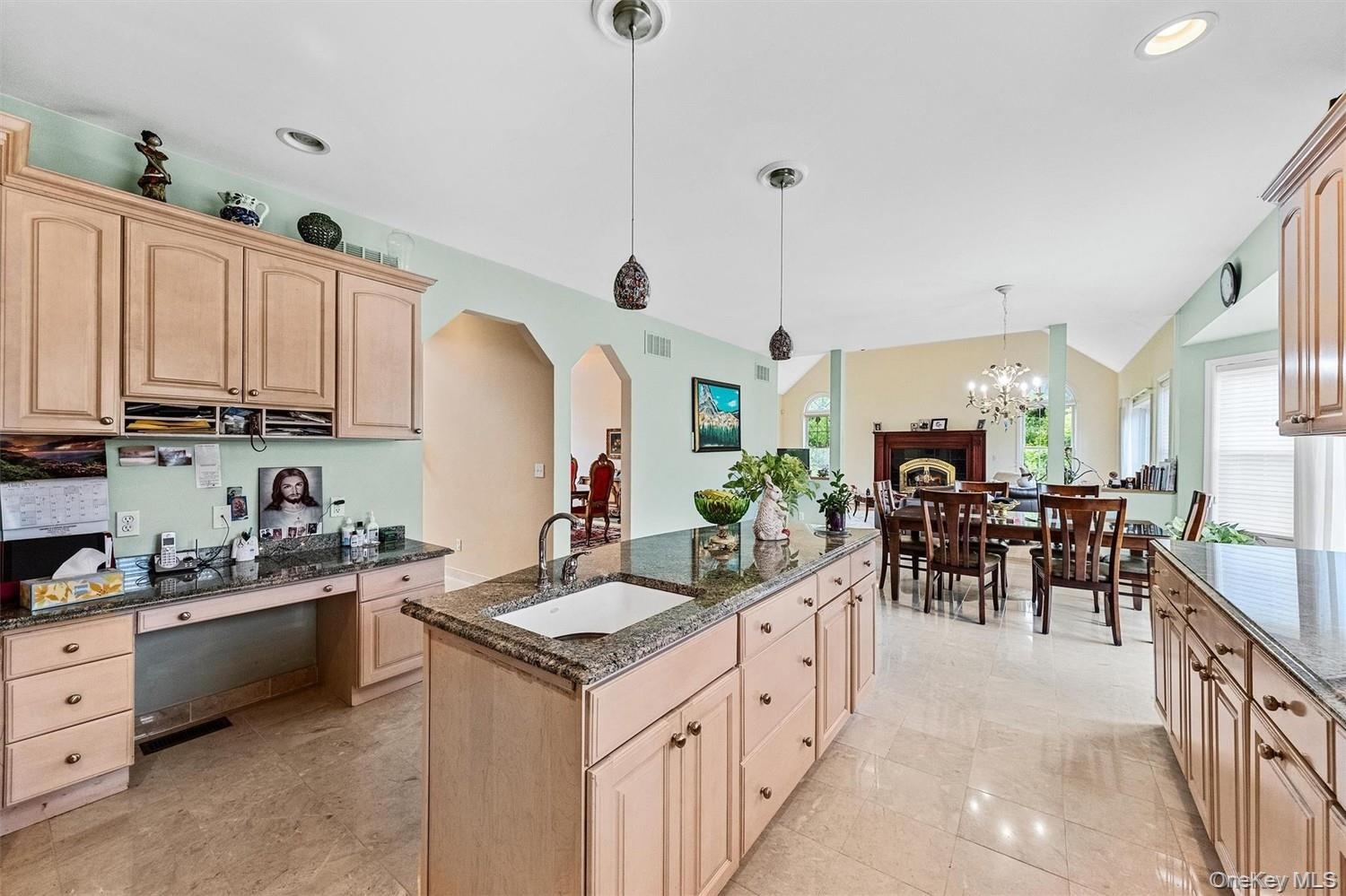 Kitchen with light wood finish cabinets, dark stone counters, arched walkways, and vaulted ceiling