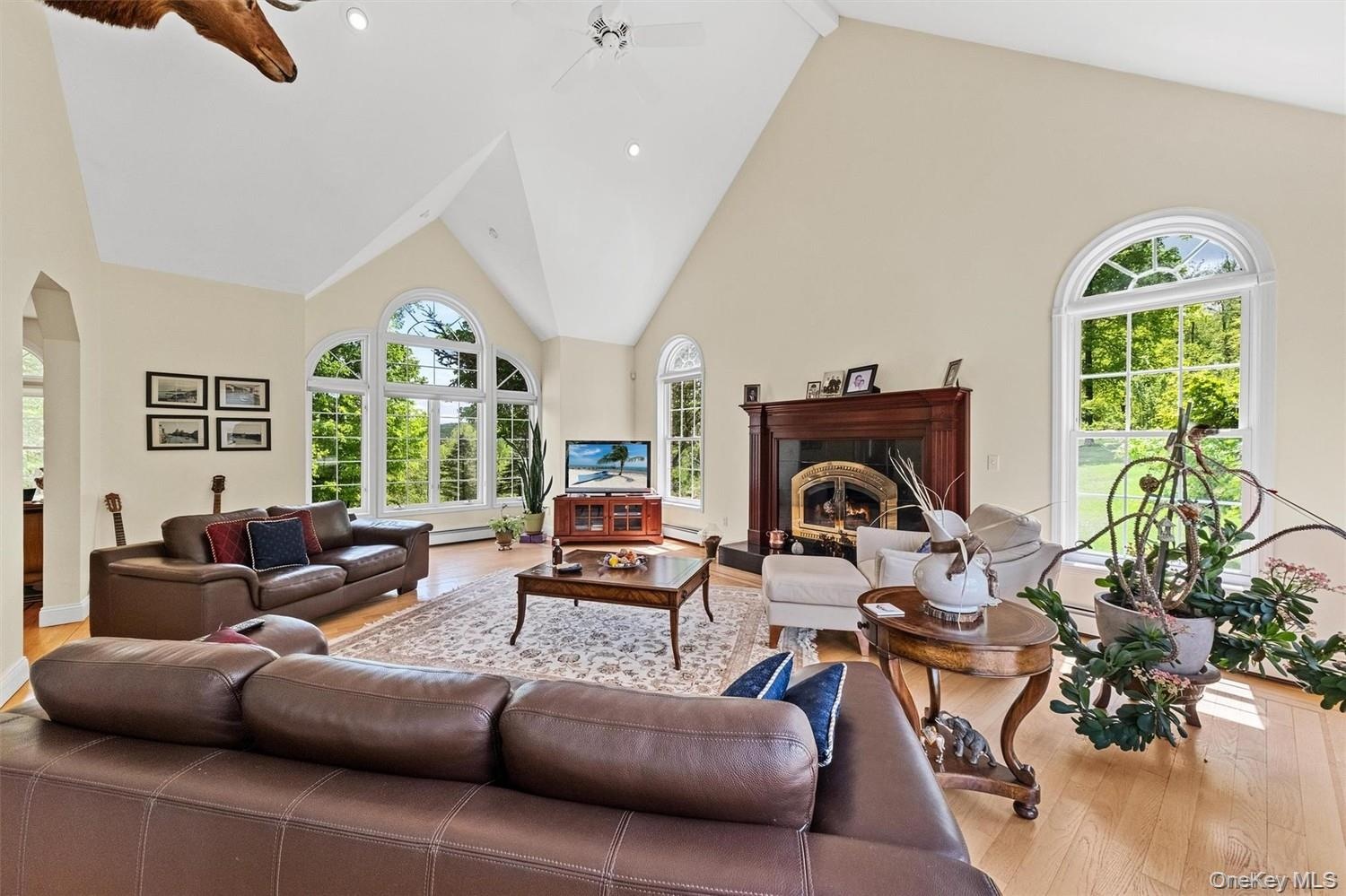 Living room with a high ceiling, light wood finished floors, a fireplace, ceiling fan, and arched walkways
