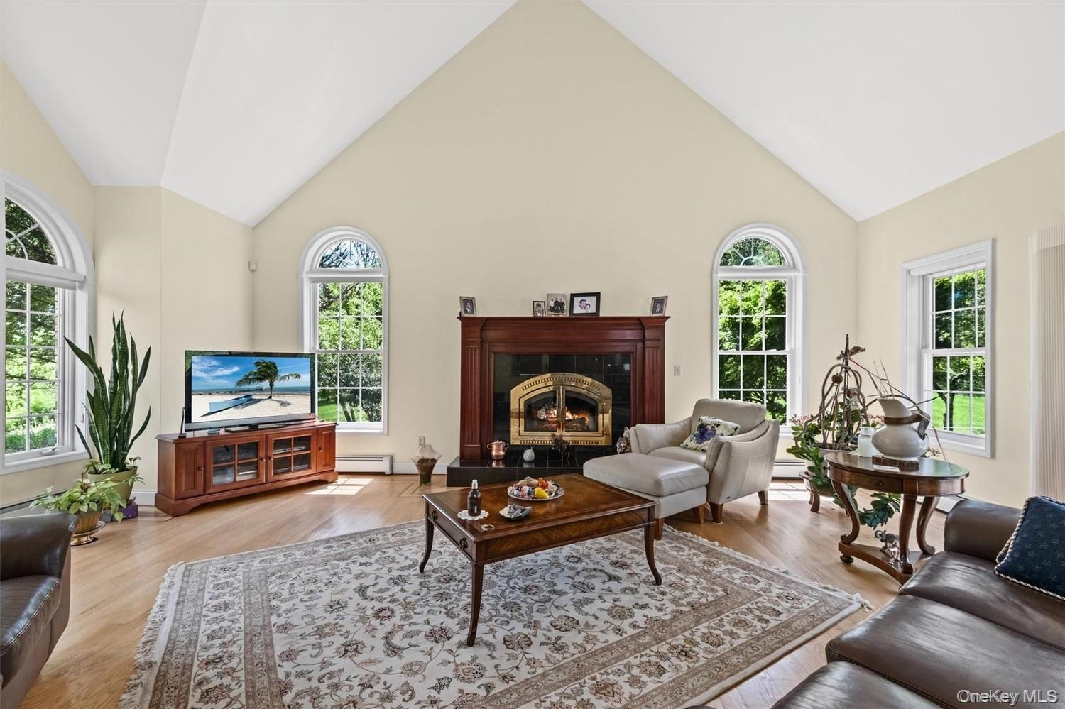 Living room with a high ceiling, light wood finished floors, baseboard heating, and a high end fireplace