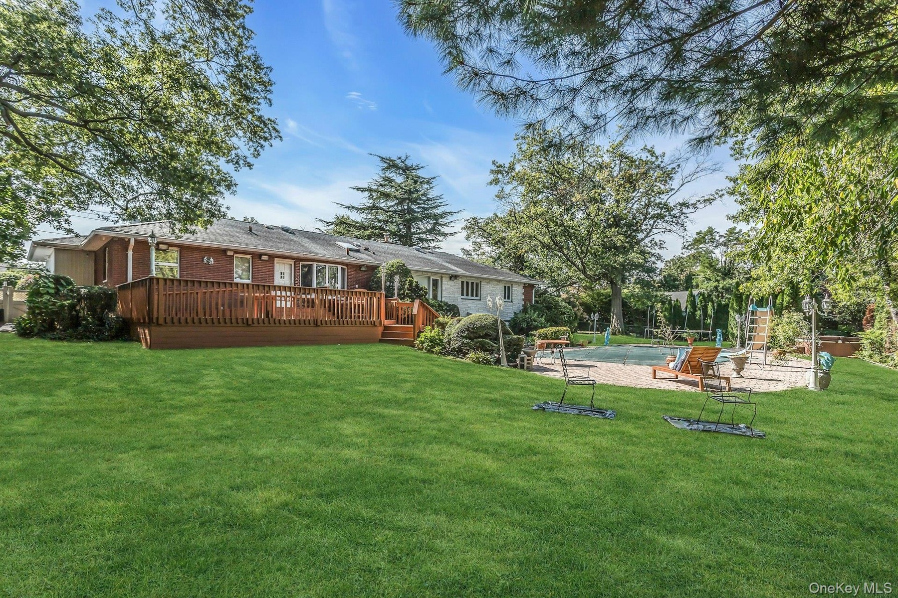 Back of house featuring an outdoor pool, a yard, brick siding, a wooden deck, and a patio area