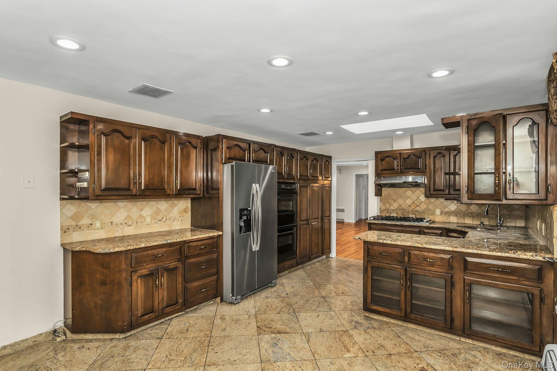 Kitchen featuring glass insert cabinets, backsplash, light stone countertops, dark brown cabinetry, and a skylight