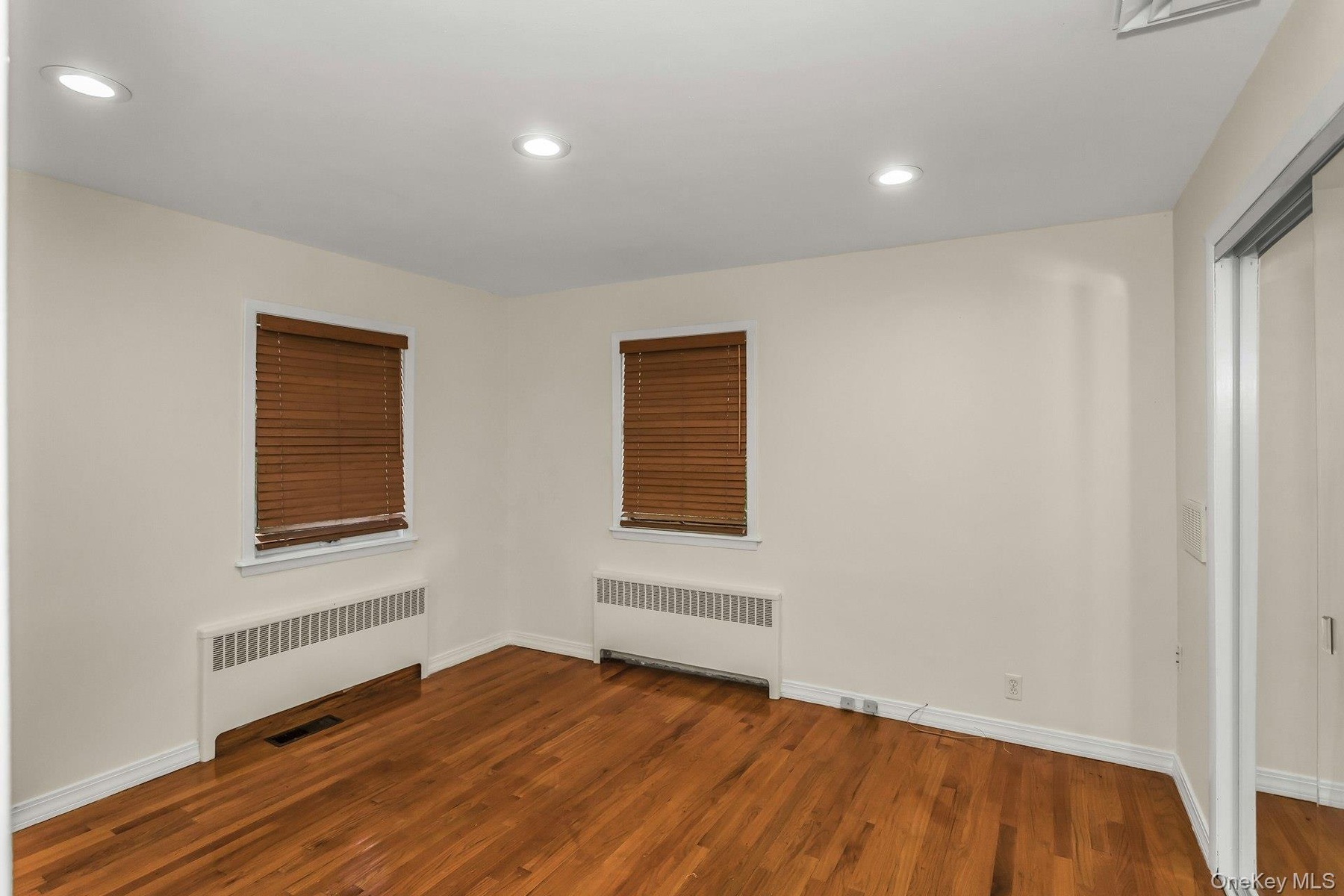 Empty room featuring radiator, wood finished floors, and recessed lighting
