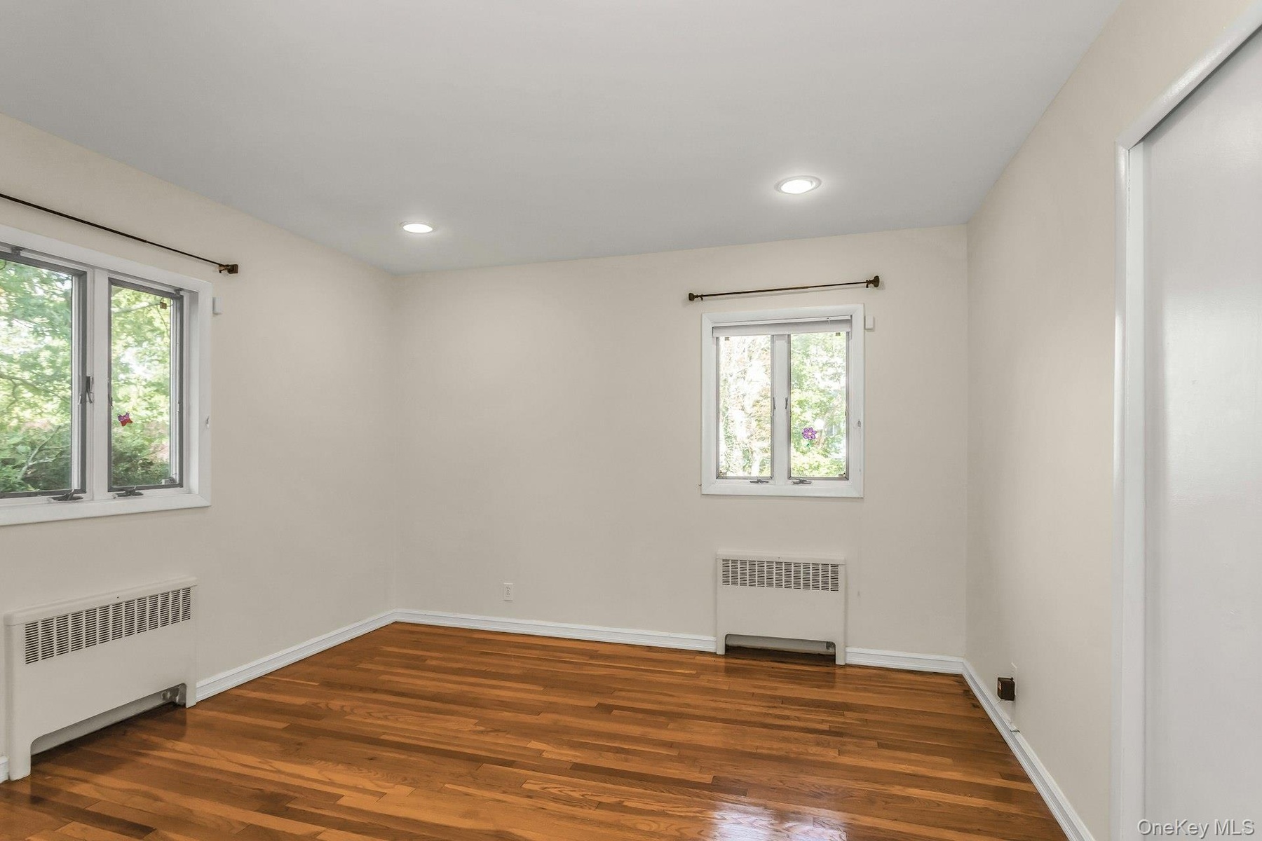 Empty room with radiator heating unit, dark wood-style flooring, and recessed lighting