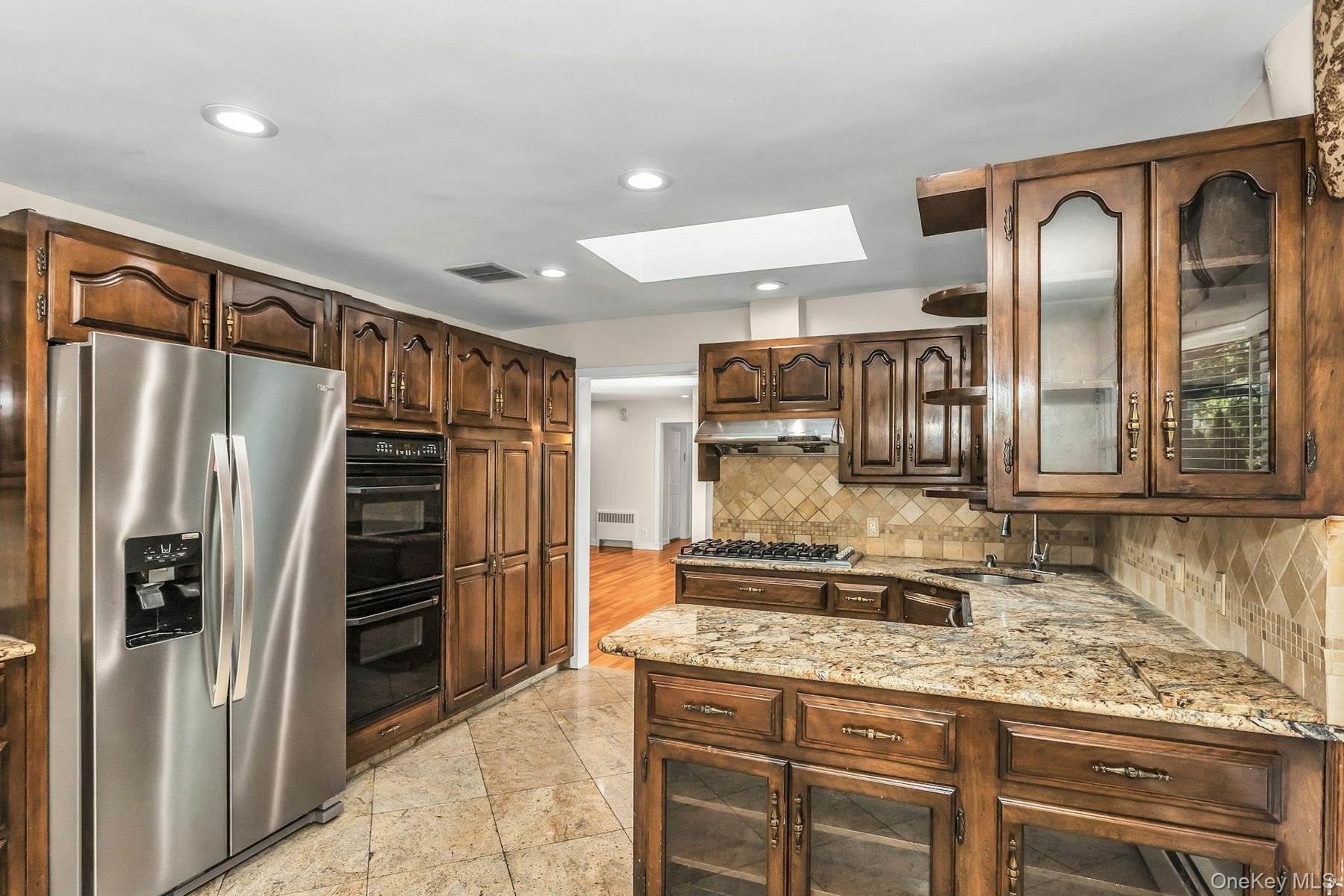 Kitchen featuring glass insert cabinets, a skylight, appliances with stainless steel finishes, recessed lighting, and light stone countertops