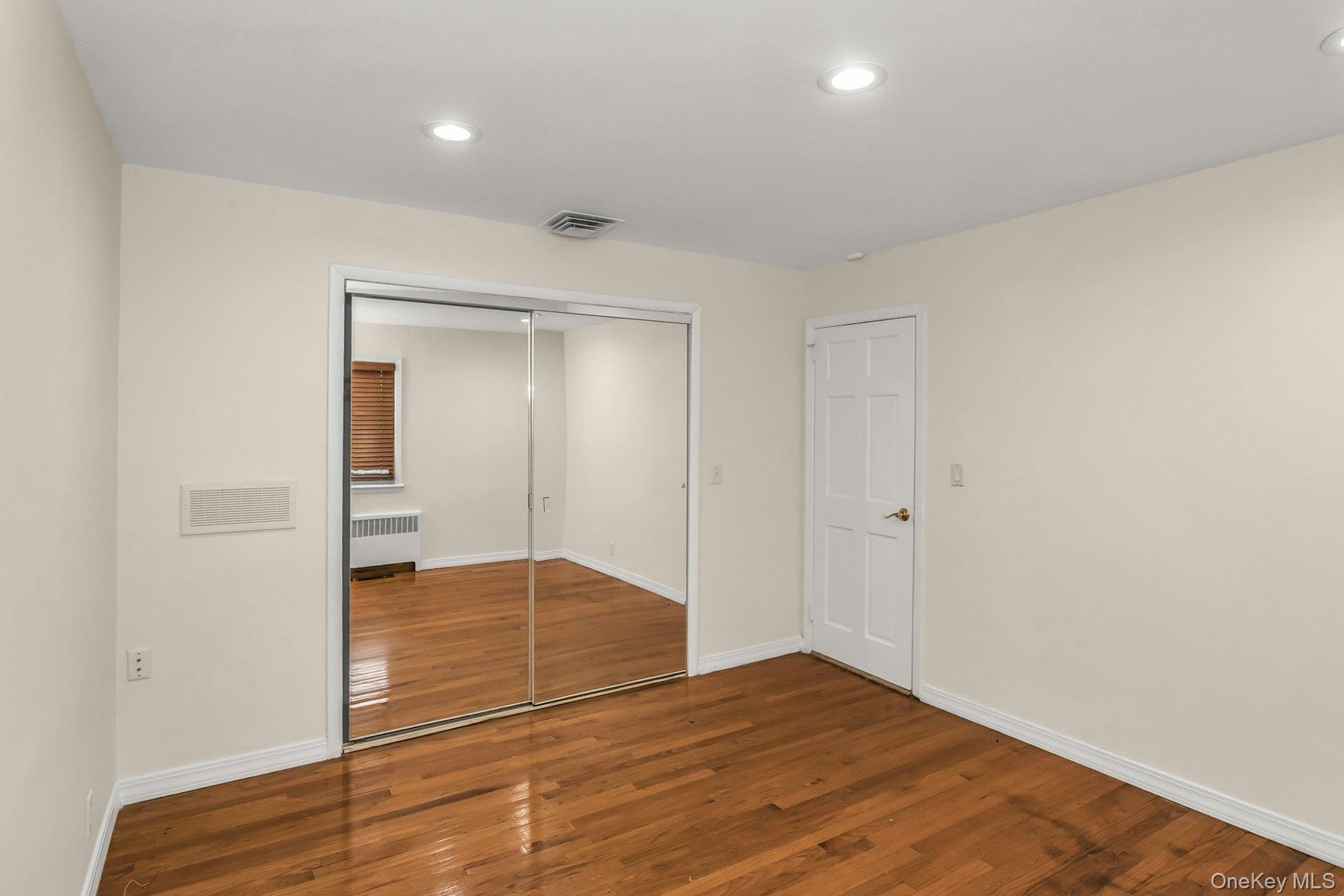 Unfurnished bedroom with wood finished floors, recessed lighting, radiator heating unit, and a closet