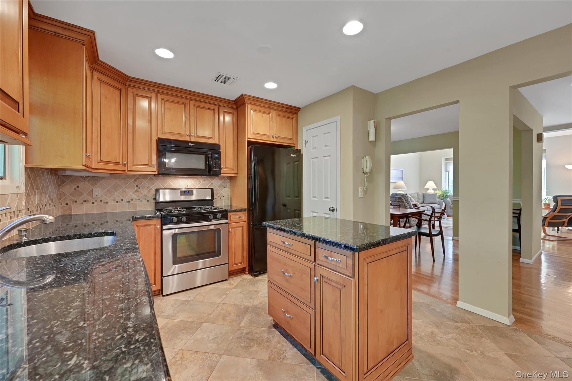 Kitchen featuring wood cabinetry, stainless steel range, built-in microwave, and a central island with a dark granite countertop
