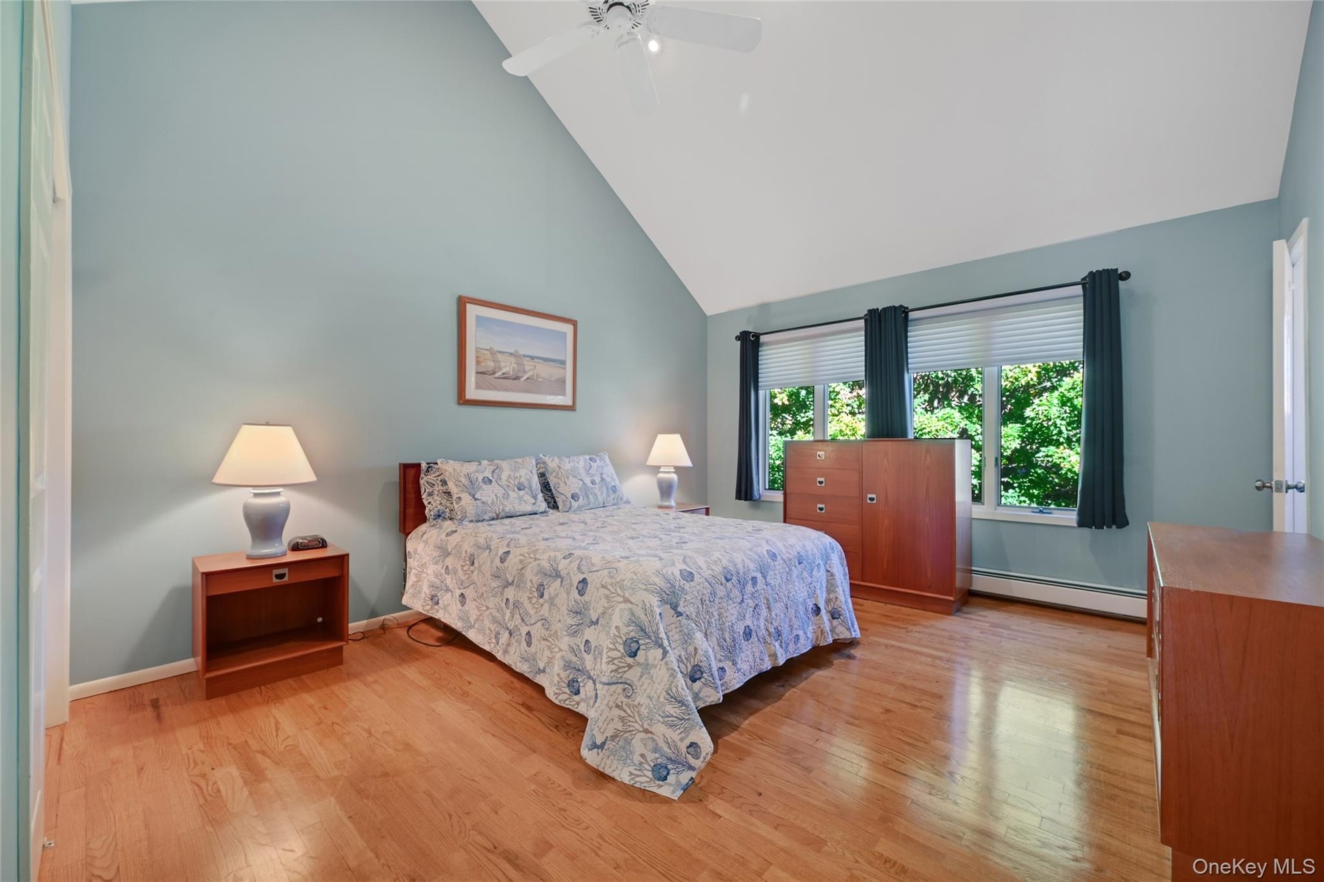Primary bedroom with vaulted ceiling, hardwood flooring, multiple windows, ceiling fan, and light-toned wall color