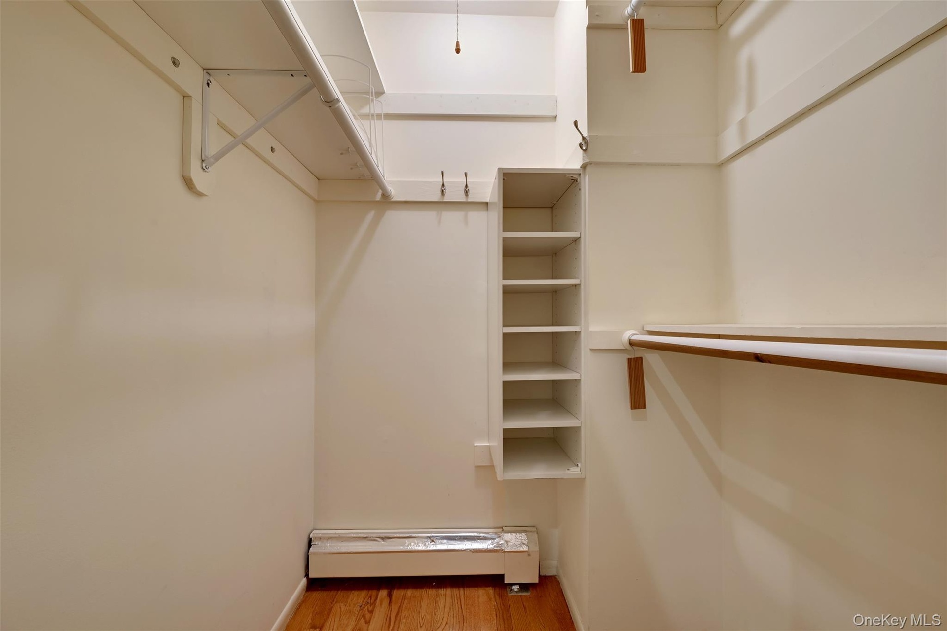 Built-in shelving, hanging rods, wood-finish flooring, and white painted walls in primary bedroom