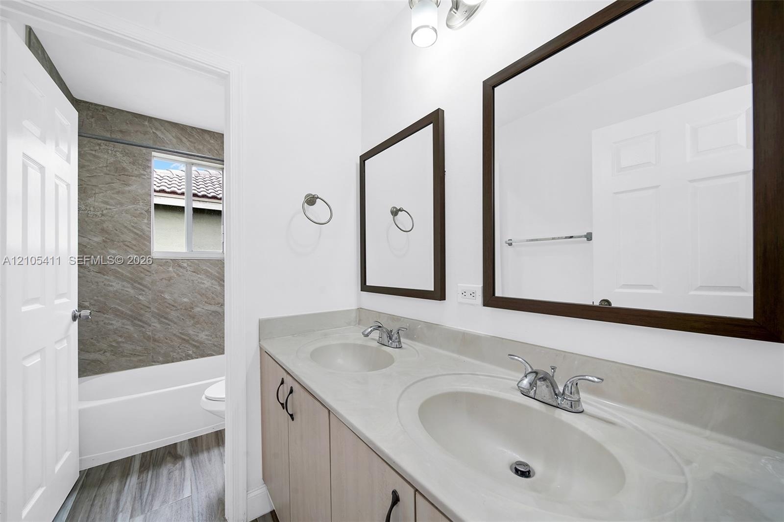 Bathroom featuring a dual vanity with integrated sinks, framed mirrors, wood-finish flooring, and a shower/tub combination with a tiled surround