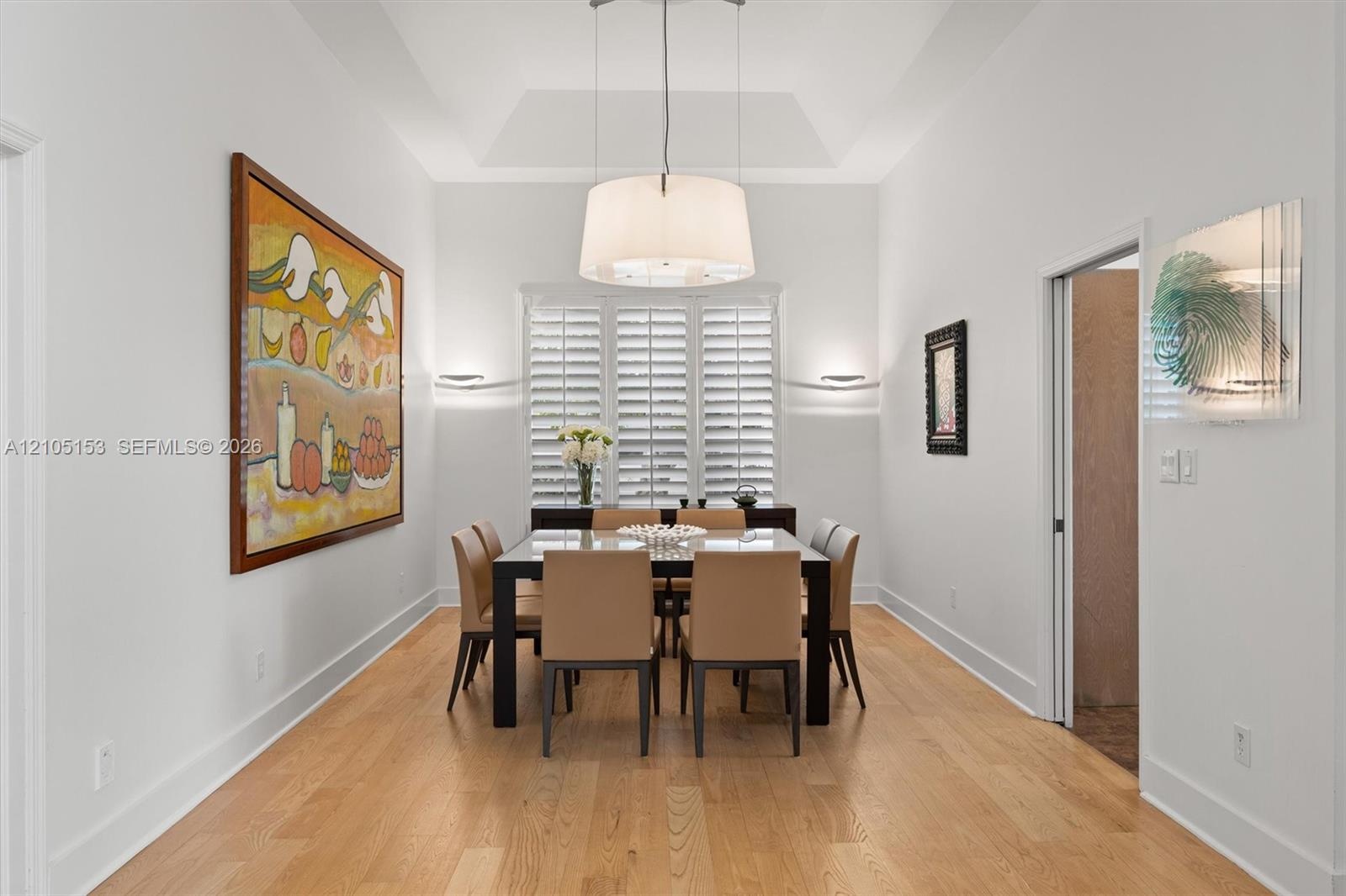 Wood-finish flooring throughout, tray ceiling, and a large window with plantation shutters