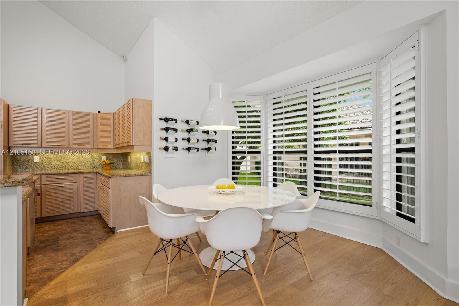 Vaulted ceiling, wood-finish flooring, bay window with plantation shutters, wood cabinetry, and granite countertops
