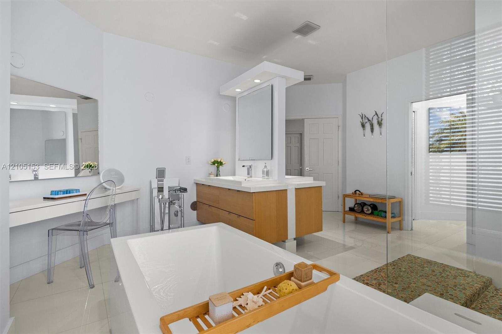 Freestanding bathtub with deck-mounted faucet, dual vanity with wood-finish cabinetry, built-in makeup vanity, glass-enclosed shower, and tiled floori