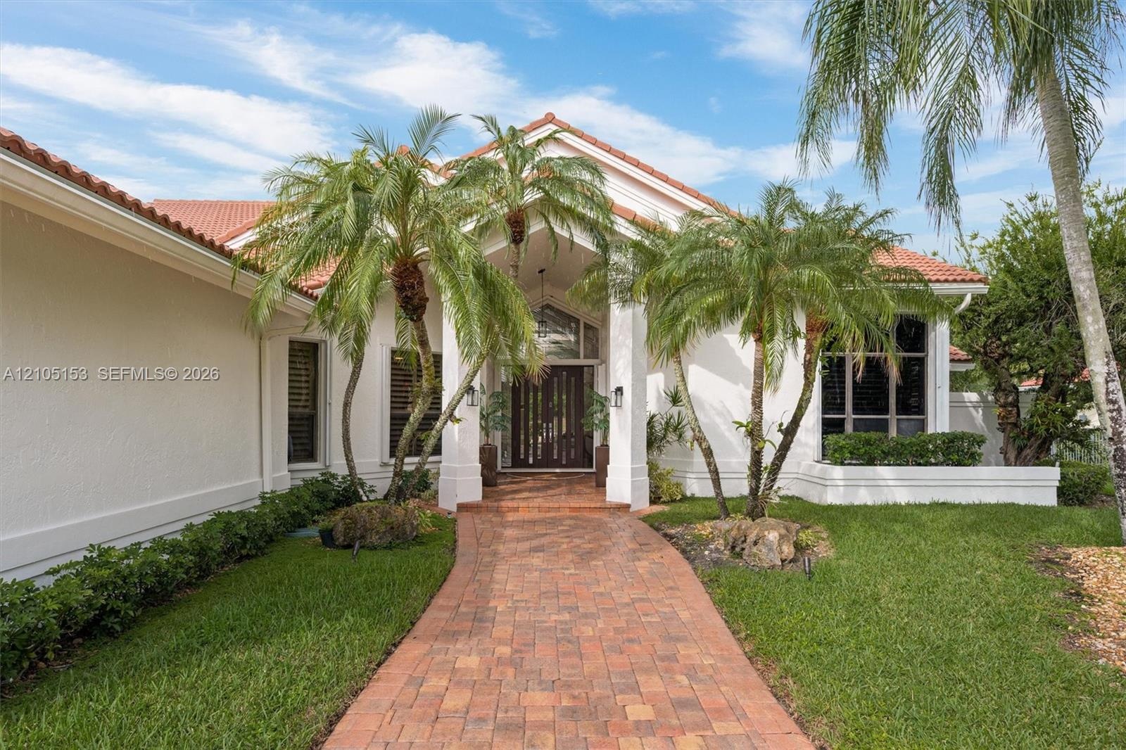 Red tile roof, stucco exterior, paver walkway, mature palm trees, and established landscaping