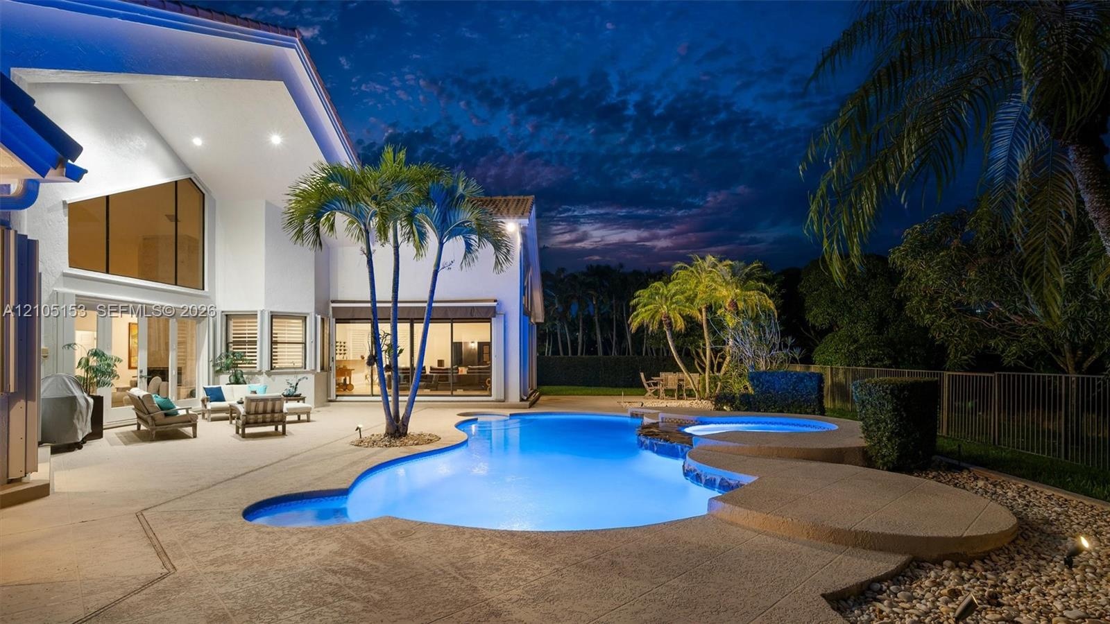 Expansive patio featuring a freeform swimming pool, integrated spa, and mature palm trees