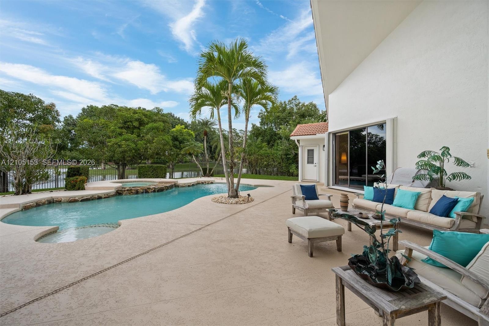 Shaped pool with integrated spa, expansive patio, mature palm trees, and sliding glass doors
