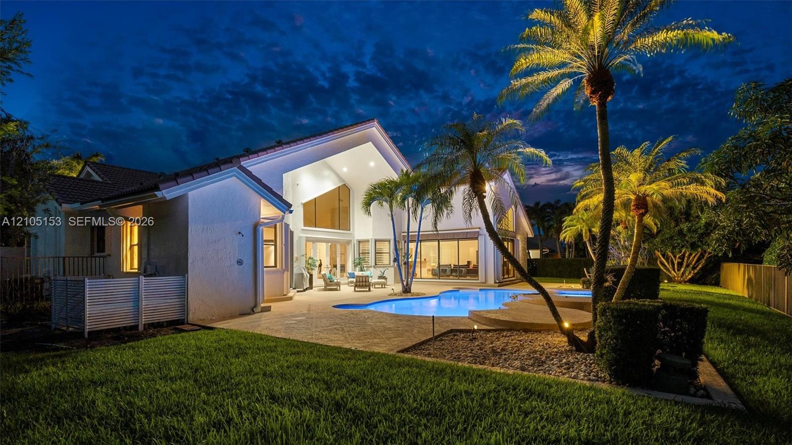 Expansive backyard featuring a manicured lawn, a swimming pool with a surrounding patio, mature palm trees, and a privacy fence