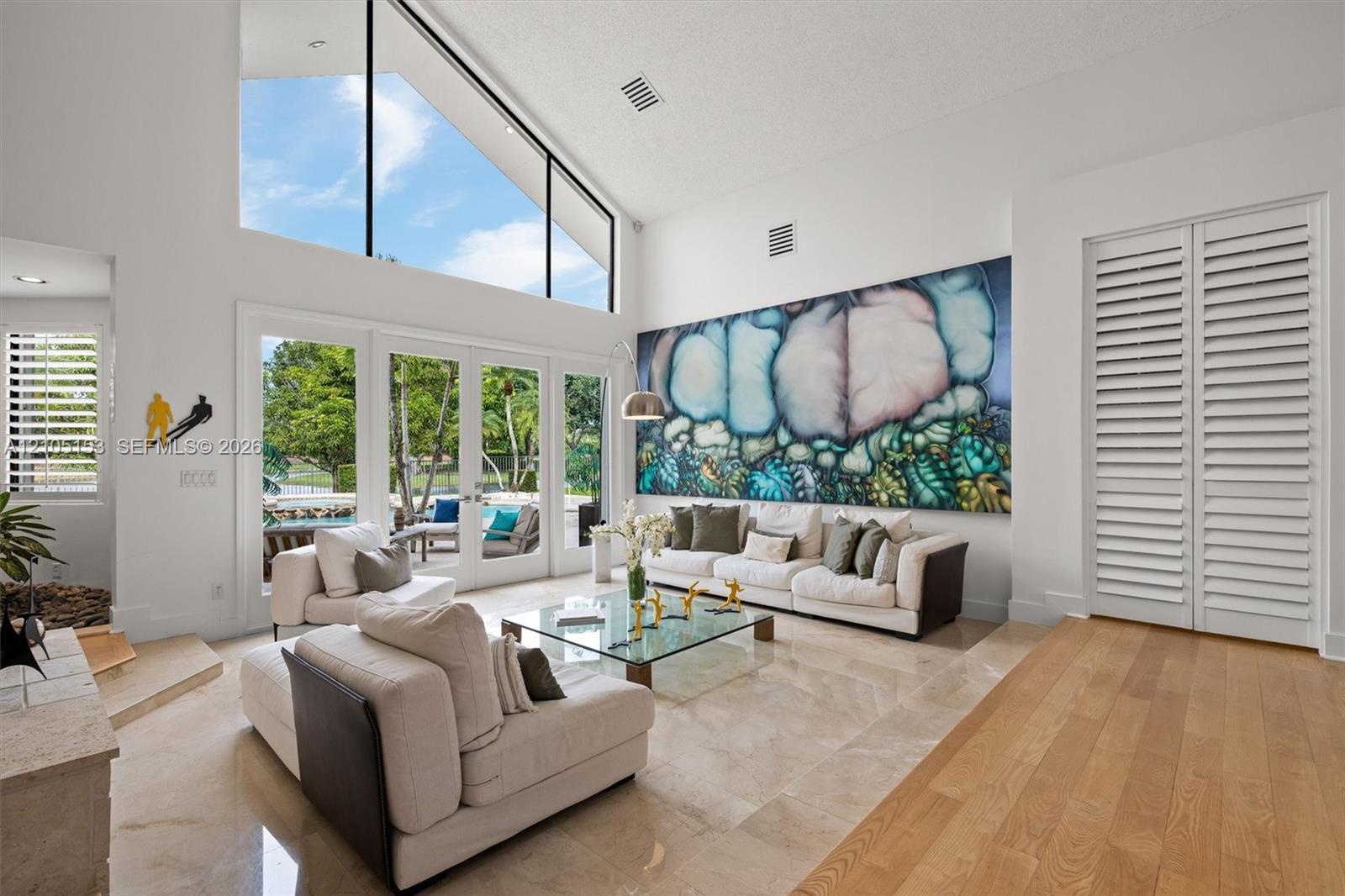 High vaulted ceiling, upper transom windows, multiple French doors, natural stone flooring, and wood-finish flooring